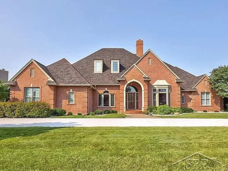 A large red brick house with multiple gabled roofs, a front porch, and a landscaped lawn.