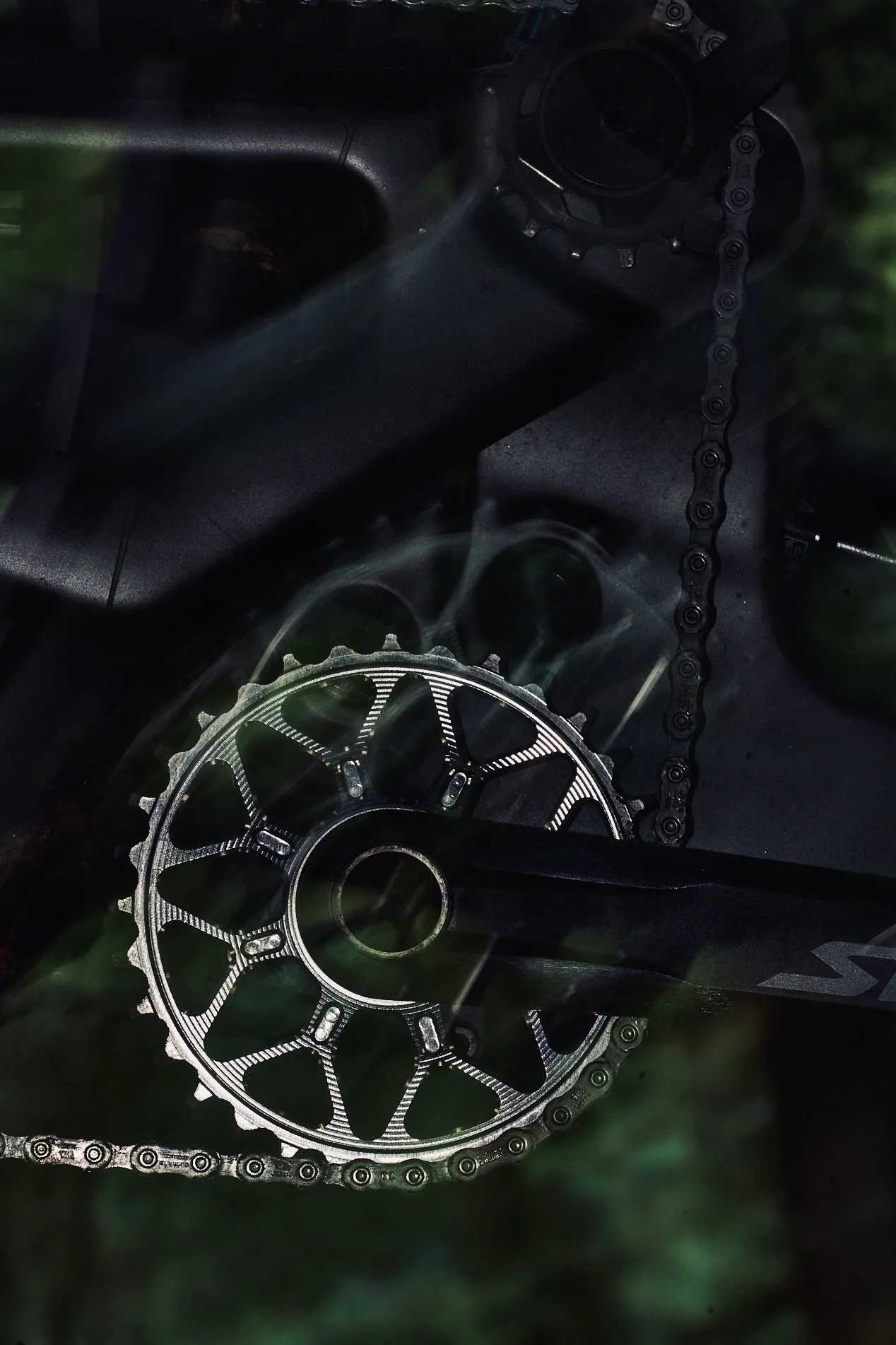 Close-up of a bicycle chainring, chain, and part of a crankset on a black bicycle frame.
