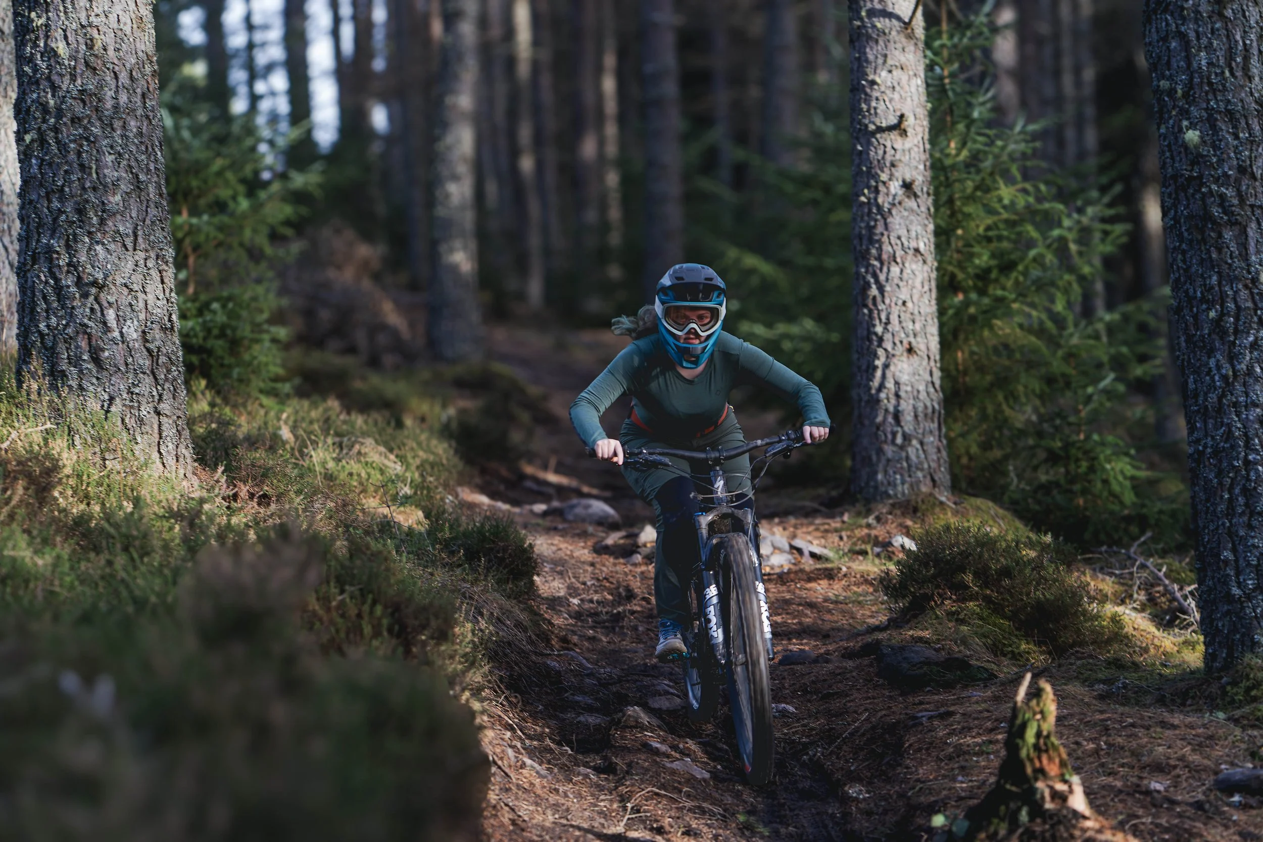 A person mountain biking through a forest trail surrounded by tall trees and green vegetation.