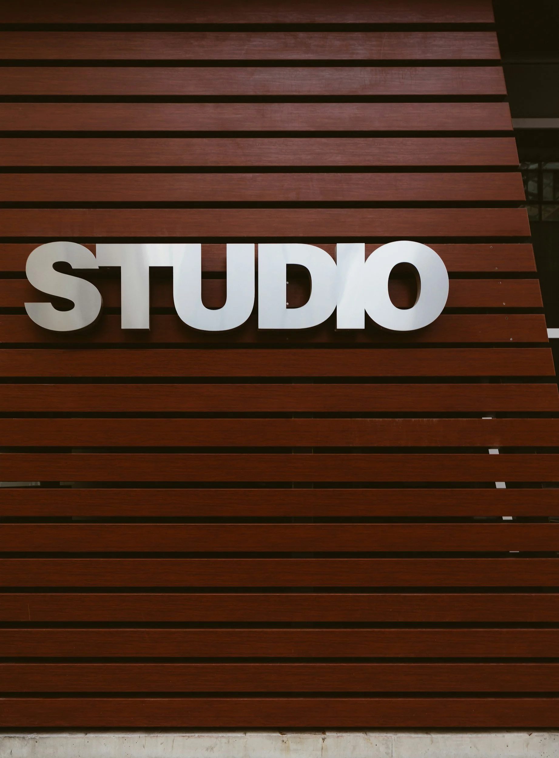 A wooden wall with dark horizontal slats and large white 3D letters spelling 'STUDO' attached to the wall.