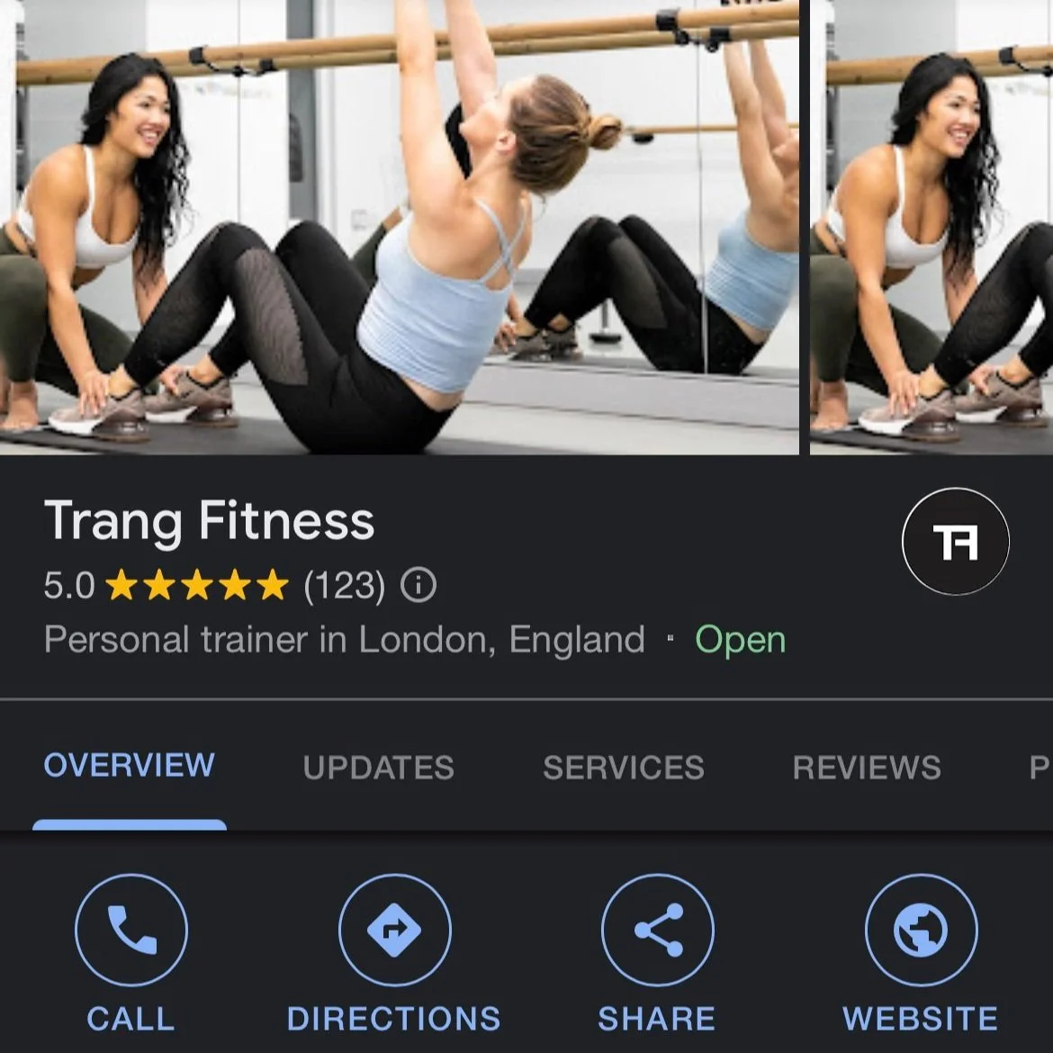 Two women at a gym with one instructing and the other performing an exercise by hanging on a wall bar, while smiling and engaging in fitness training.