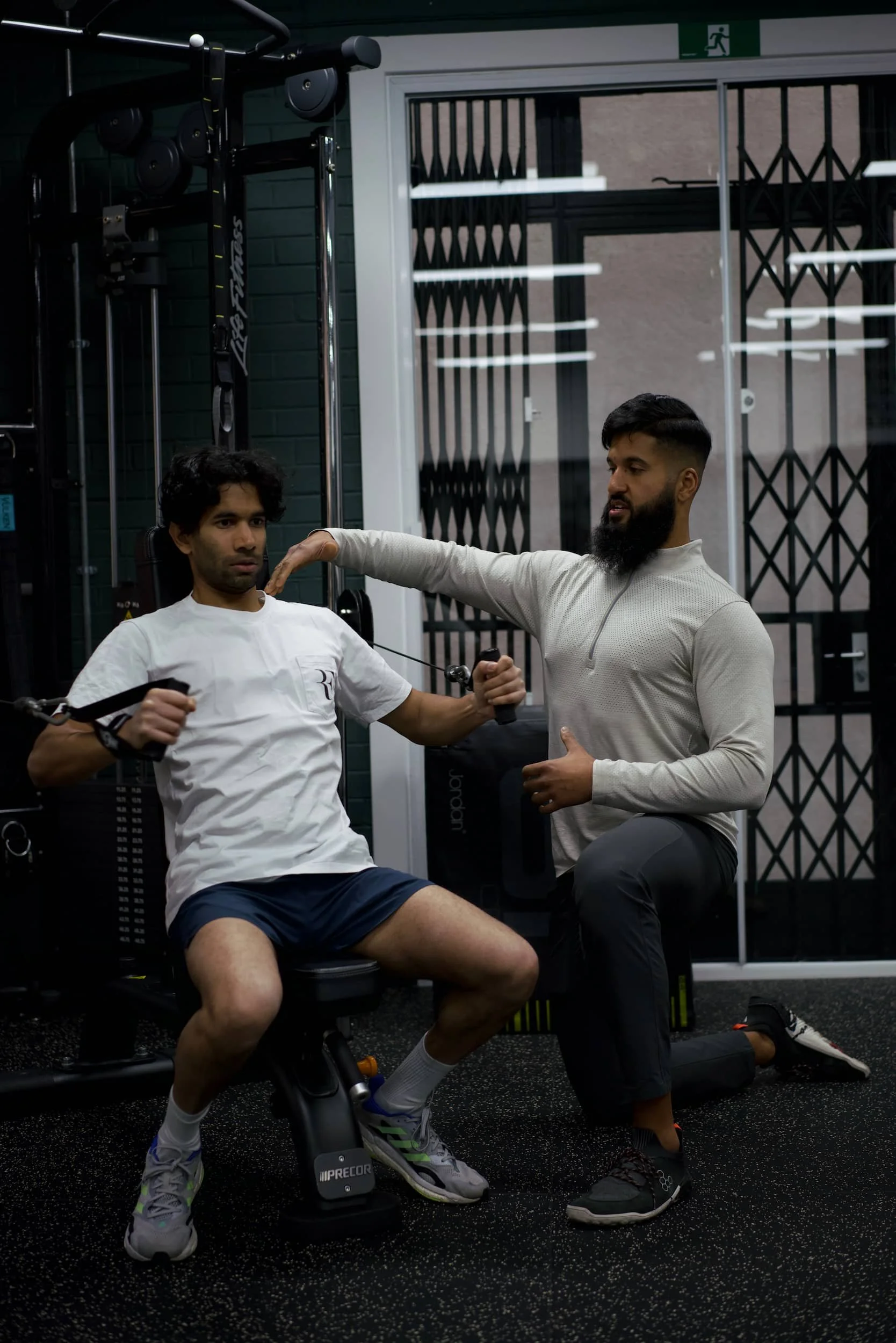 A personal trainer assisting a man with resistance band exercises during a workout session in a gym.