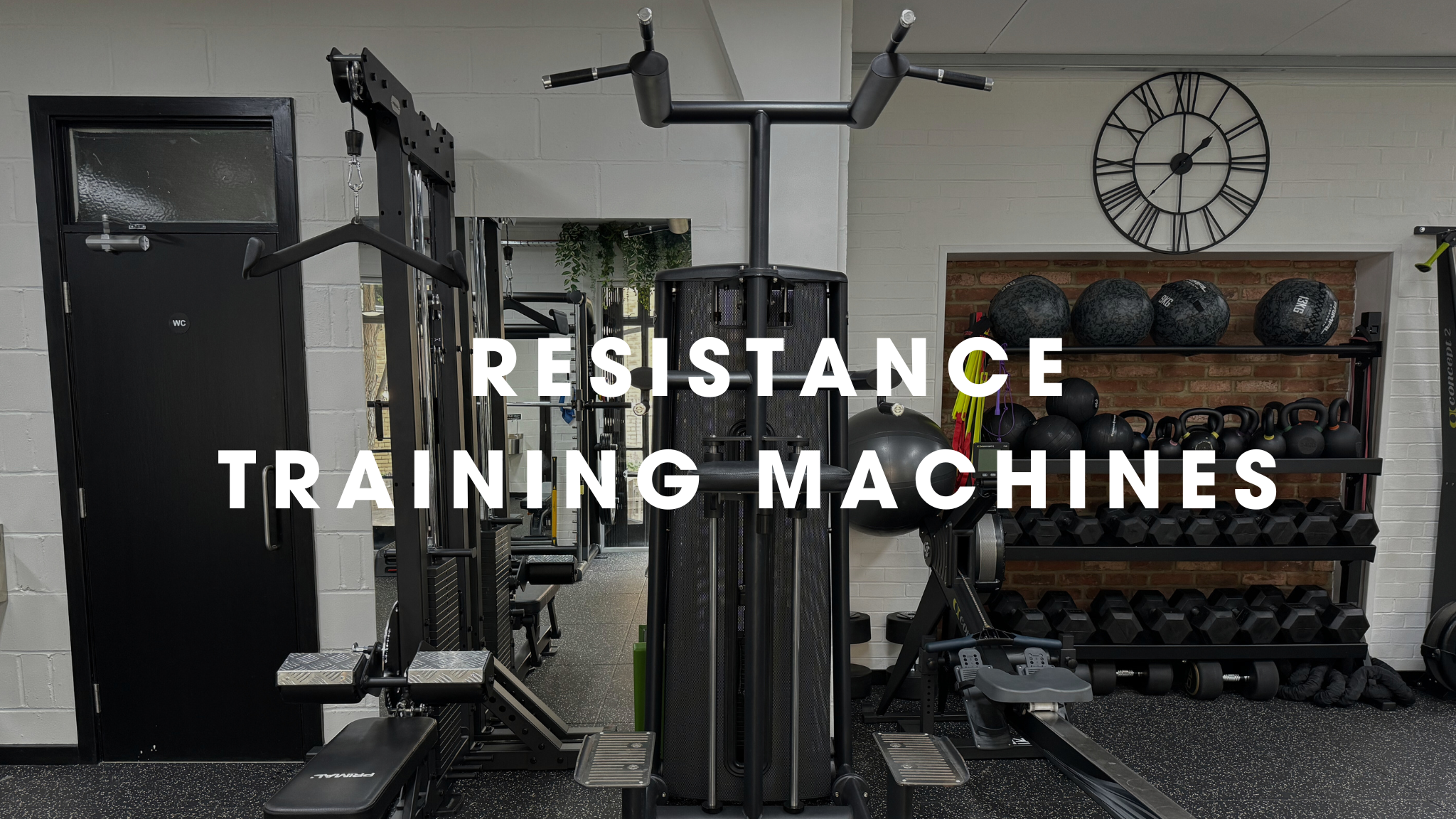 Fitness gym with resistance training machines, kettlebells, medicine balls, and wall clock.