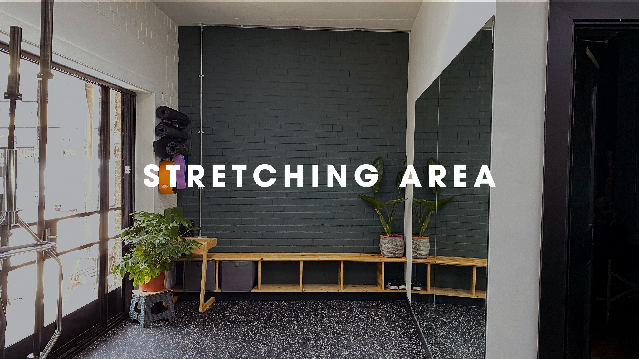 Indoor fitness stretching area with a black brick wall, a mirror, potted plants, and workout equipment.