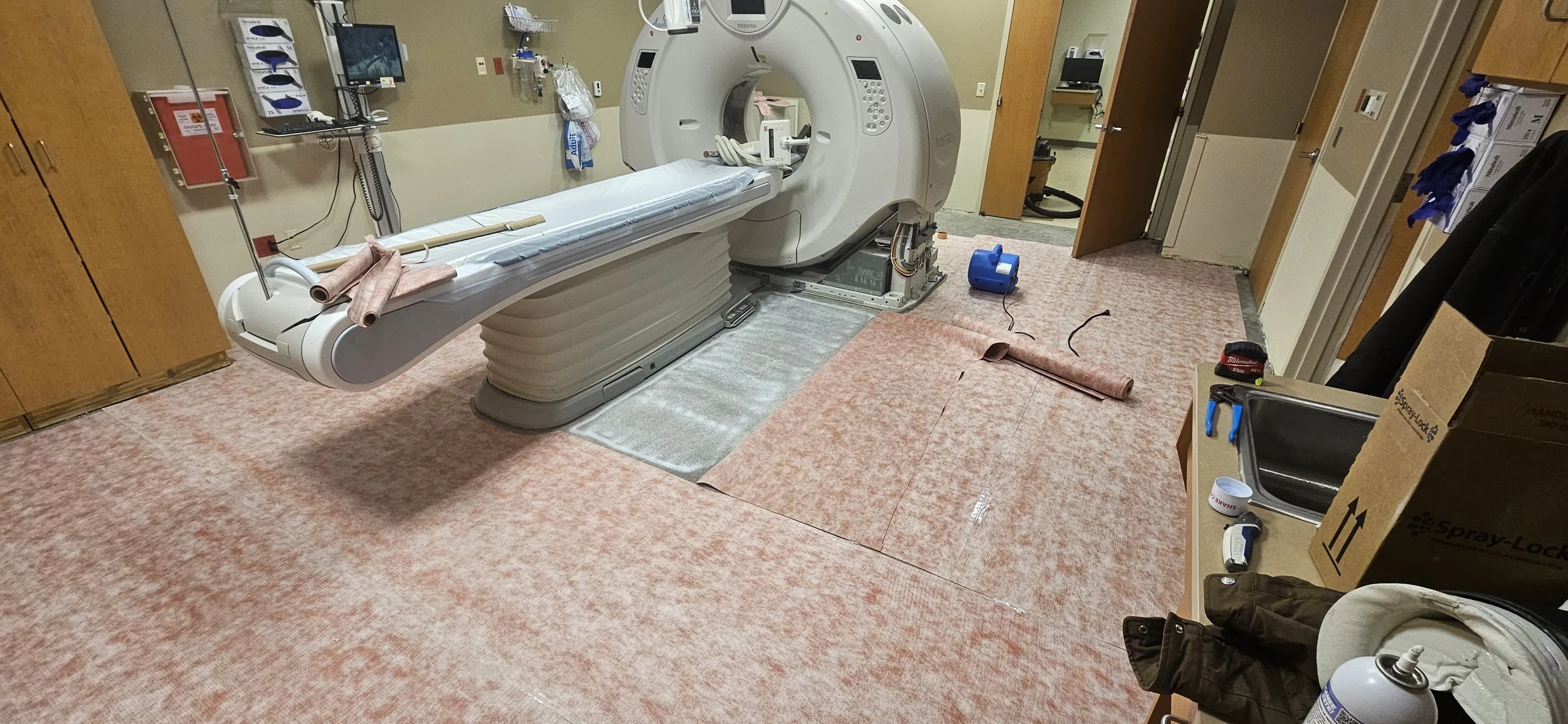 Hospital room with a large MRI machine, a long patient bed, medical supplies, and equipment, with some items on the floor and countertop.