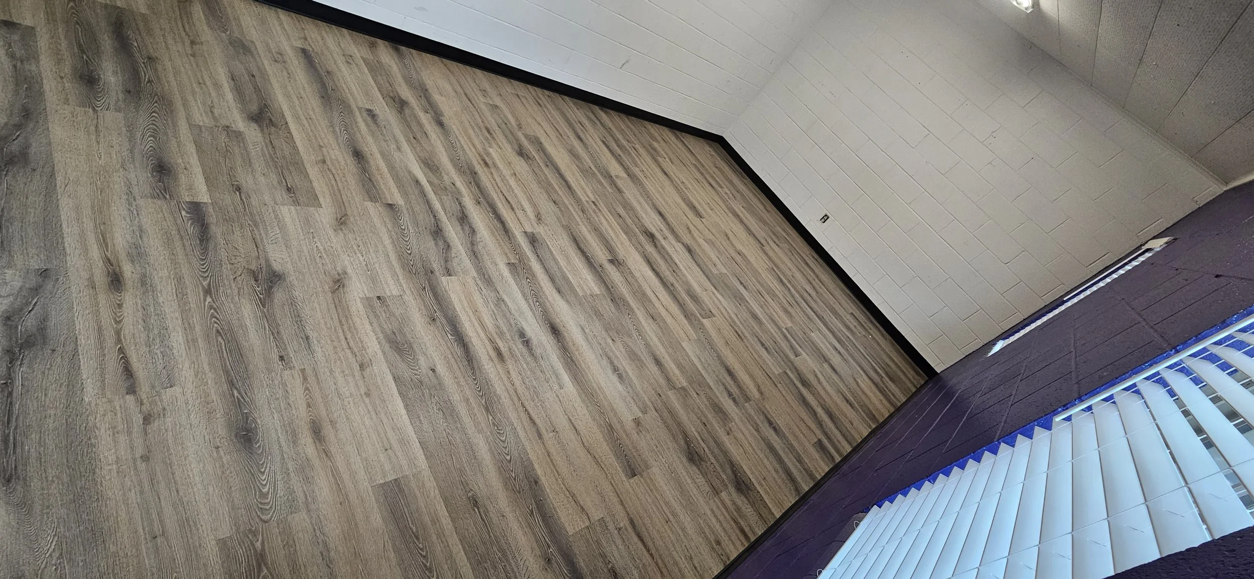 Empty indoor room with light wood flooring, white brick walls, and a window with blue blinds.