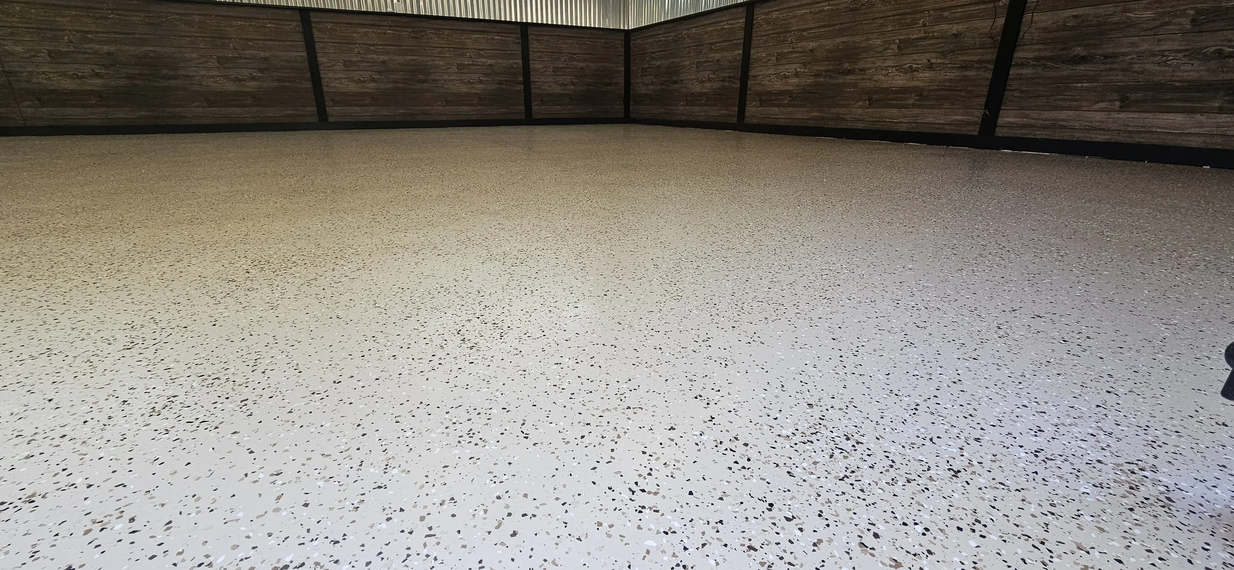 An indoor room with a speckled epoxy floor, wood-paneled walls, and black metal trim at the corners.