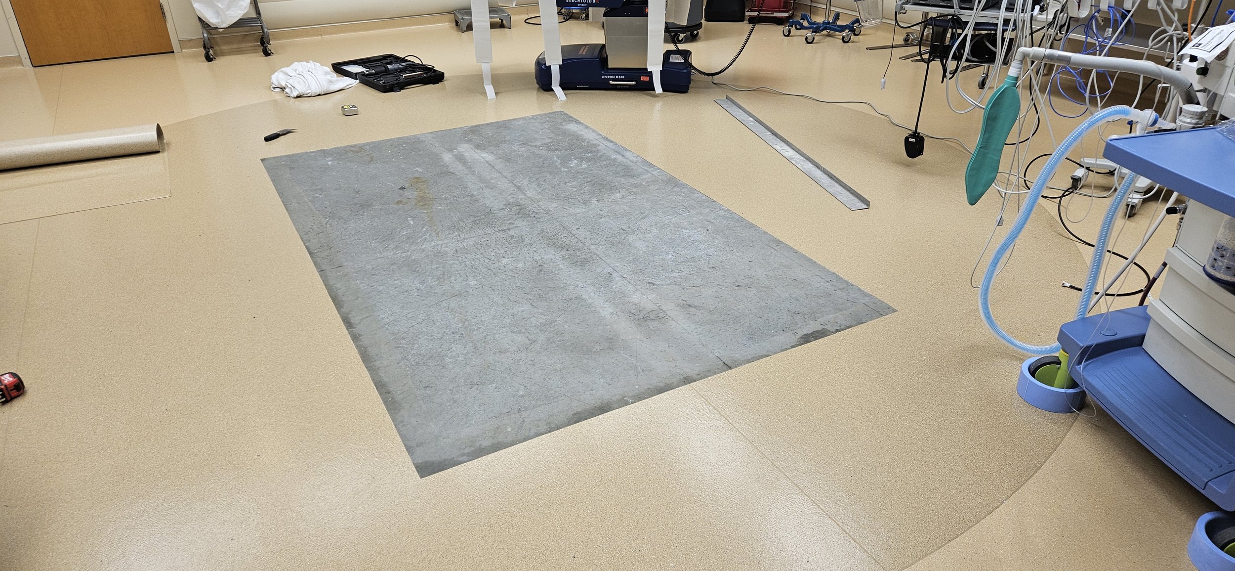 Medical room with a square area taped off on the beige floor, surrounded by various medical equipment and tools.