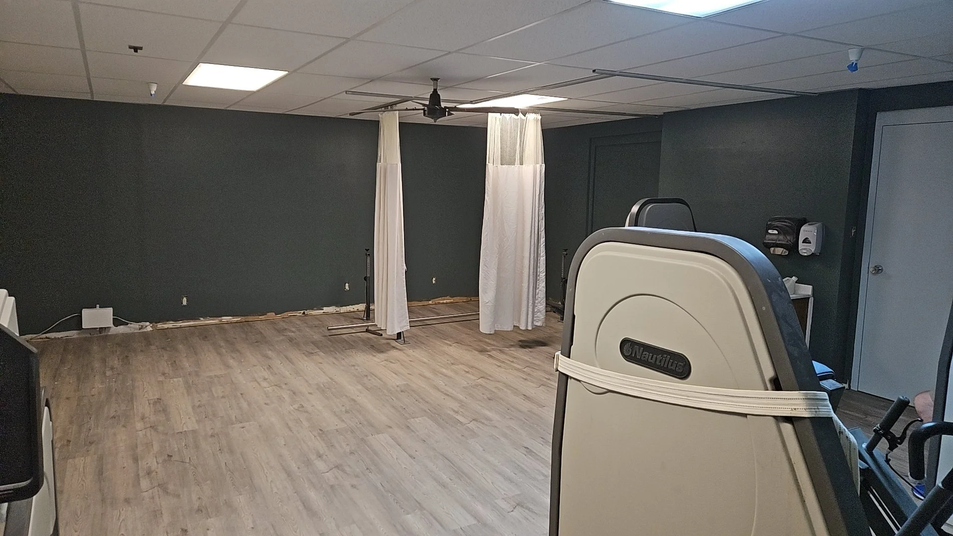 Empty hospital room with privacy curtains, medical equipment, and a ceiling fan.