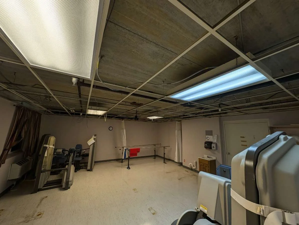 Empty physical therapy or rehabilitation room with exercise equipment, a gait belt, and medical supplies against the wall.