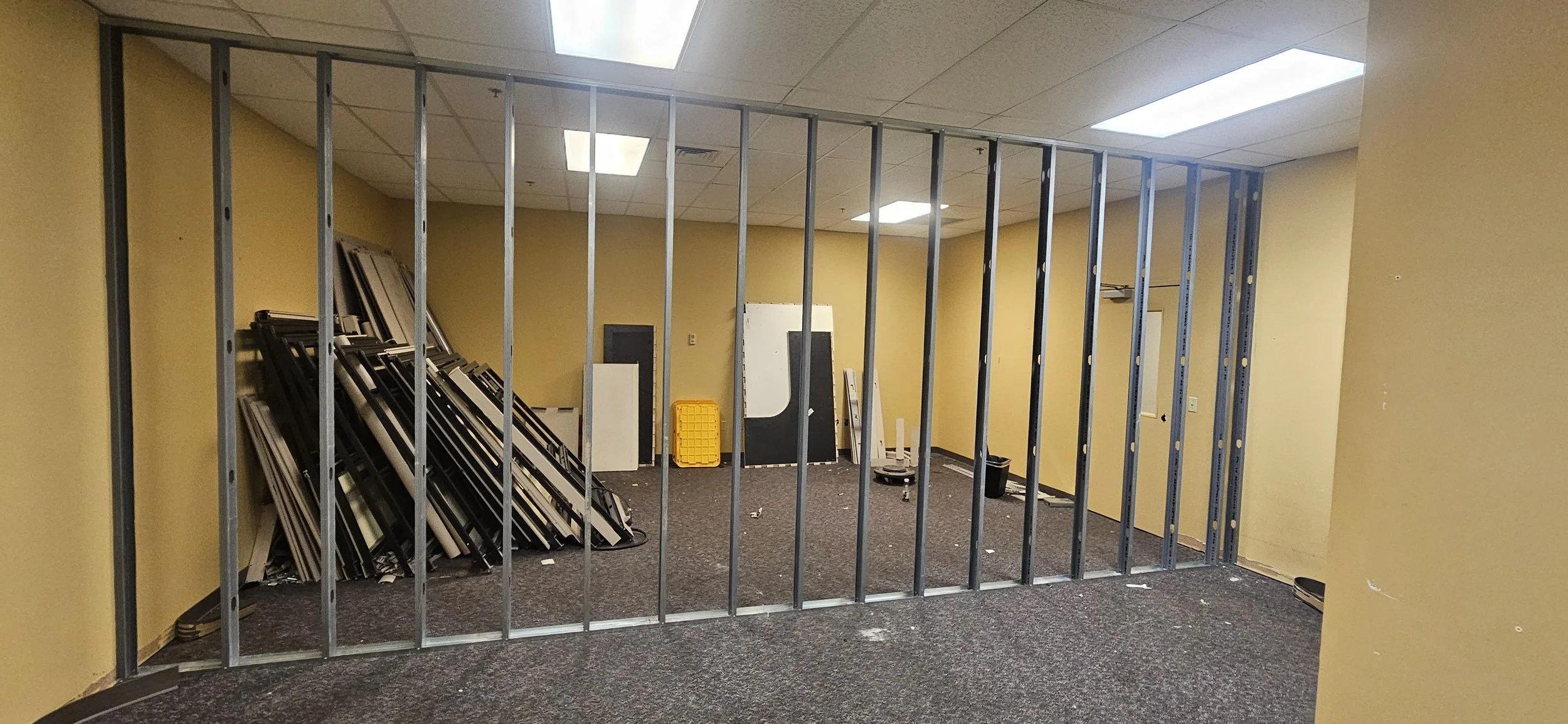 Empty office space under construction with metal framing, yellow walls, stacked window frames, and construction materials.