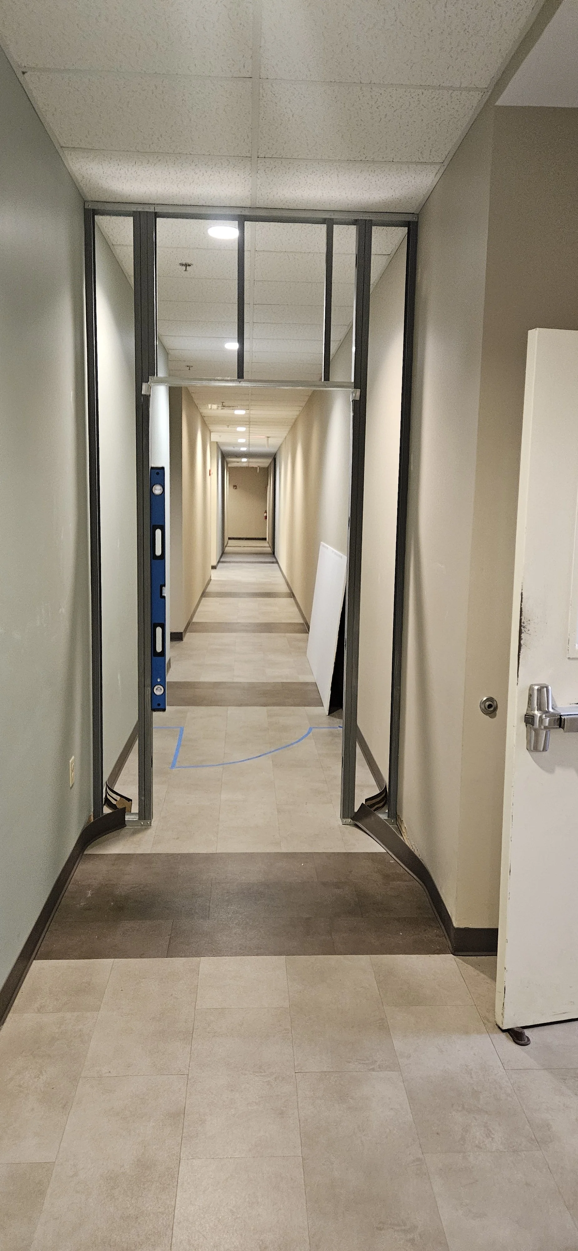 Hallway in a building under construction with metal framing, partially completed walls, and a tiled floor.