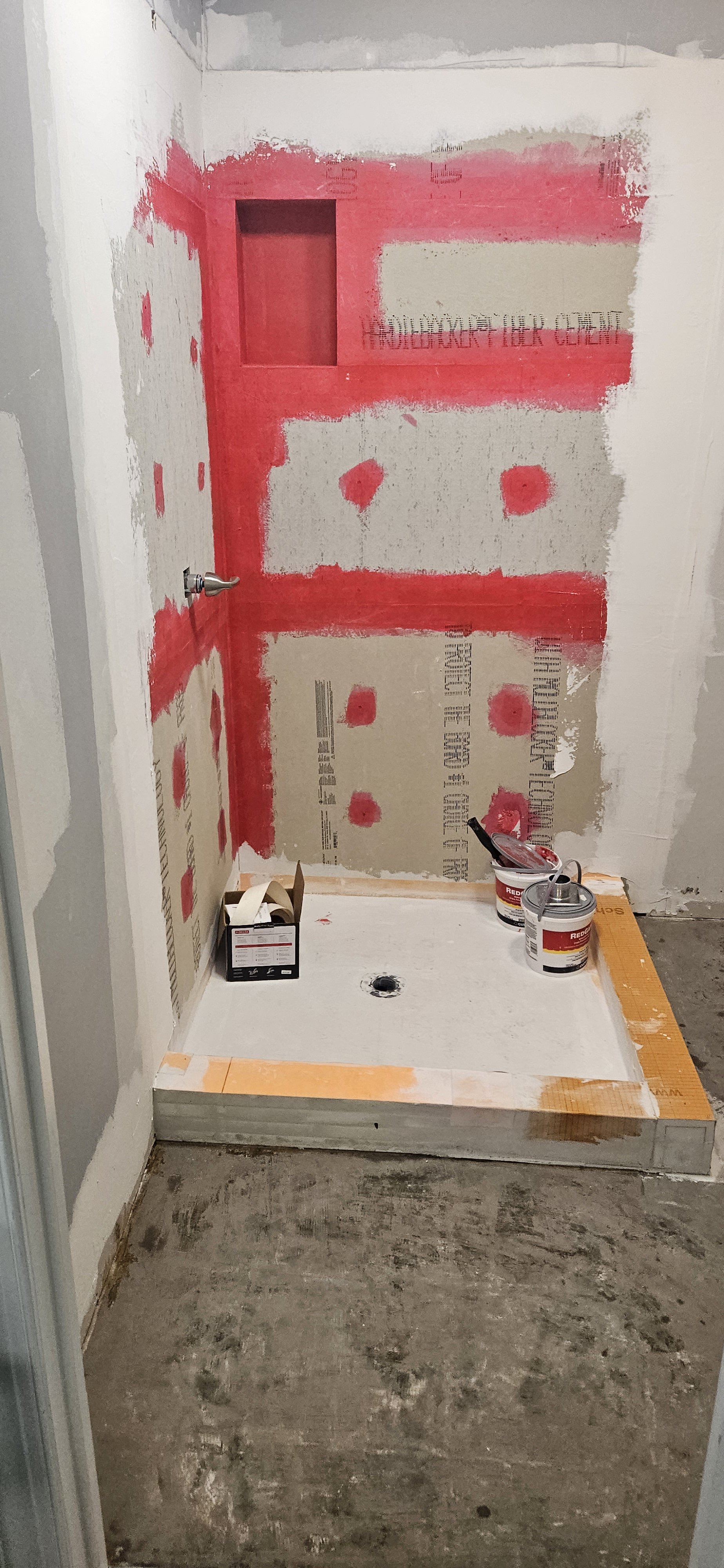 Bathroom under construction with drywall partially painted and supplies on the floor.