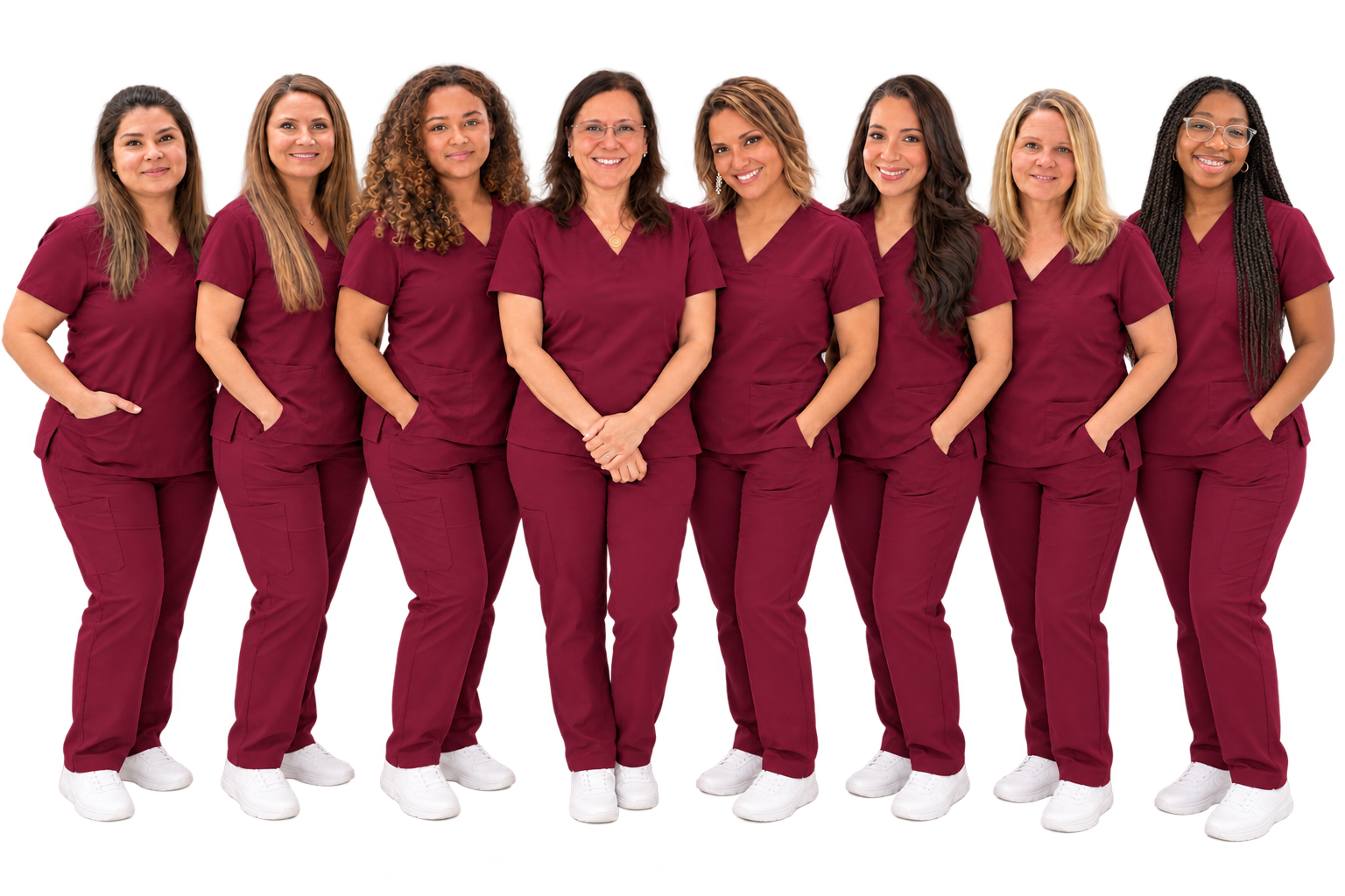 A diverse group of nine women wearing matching maroon scrubs and white sneakers, standing together against a black background.