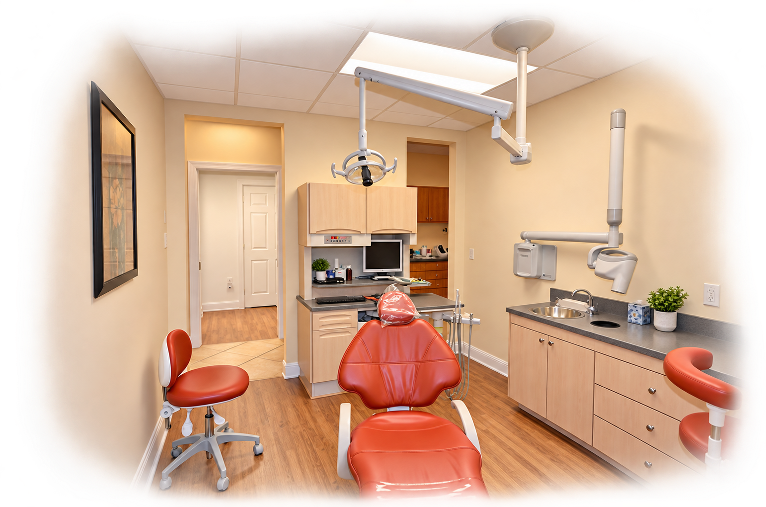 A dental examination room with dental chairs, overhead lights, and medical equipment, including x-ray machinery and a computer. The room has wood flooring, light-colored walls, and cabinetry, with a small sink and potted plant on the countertop.