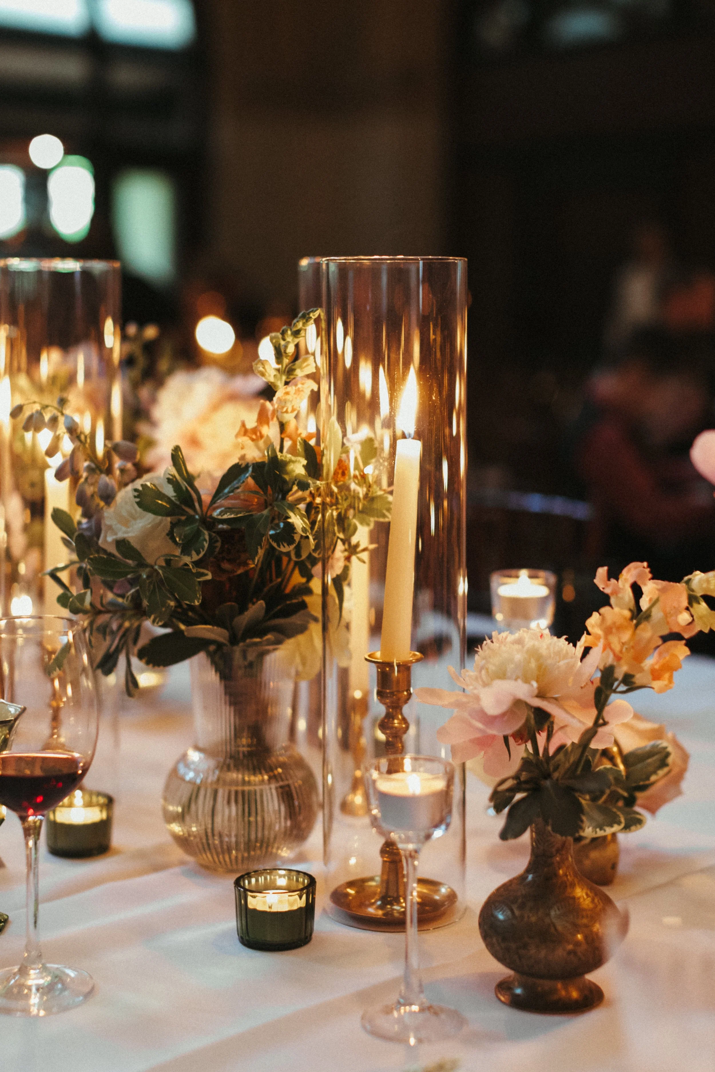 A table decorated with flowers, candles, and tall glass candle holders, creating a warm and elegant atmosphere.