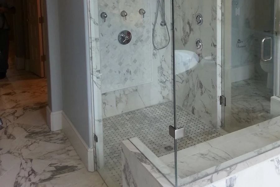Luxury marble-tiled walk-in shower with glass doors, rainfall showerhead, body jets, and mosaic floor