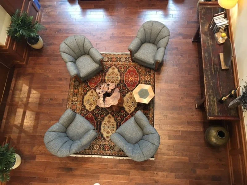 Overhead view of four gray armchairs surrounding a patterned oriental rug and coffee table in a wood-floored living room