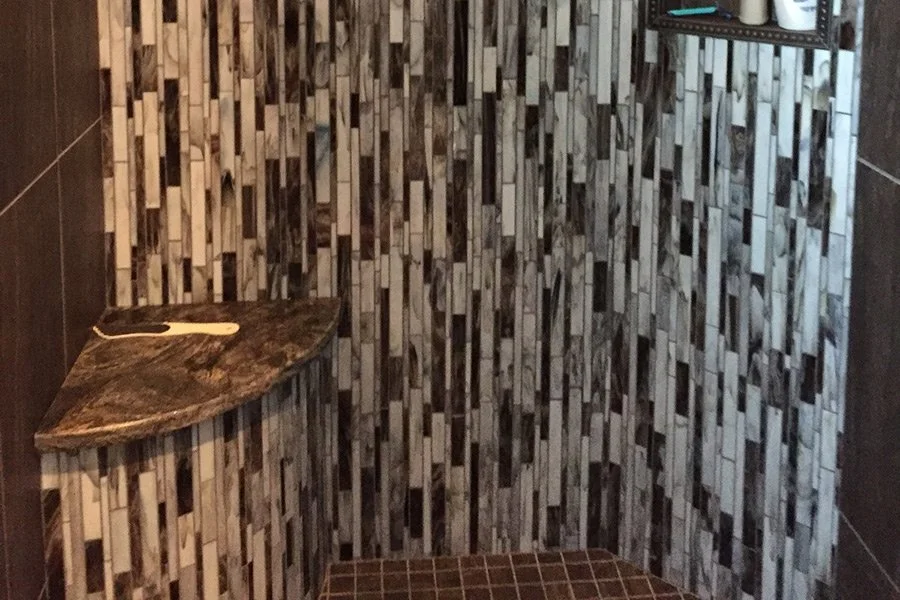 Small tiled bathroom with a corner shelf holding a wooden toilet brush and a dark tiled bench