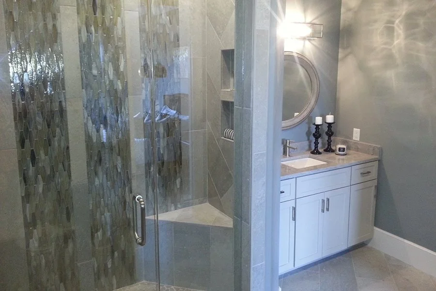 Modern bathroom with a glass-enclosed tiled shower, white vanity, round mirror, and black candleholders