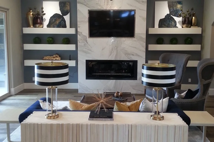 Modern living room with wall-mounted TV, marble fireplace, built-in shelves, striped table lamps, and navy sofa