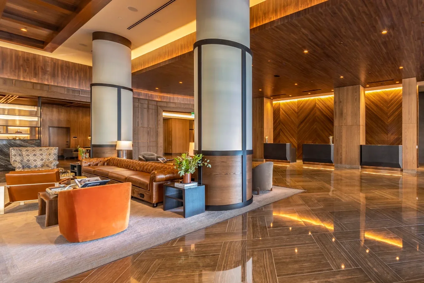 Upscale hotel lobby with leather seating, illuminated wood-paneled walls, large columns, and polished marble floors