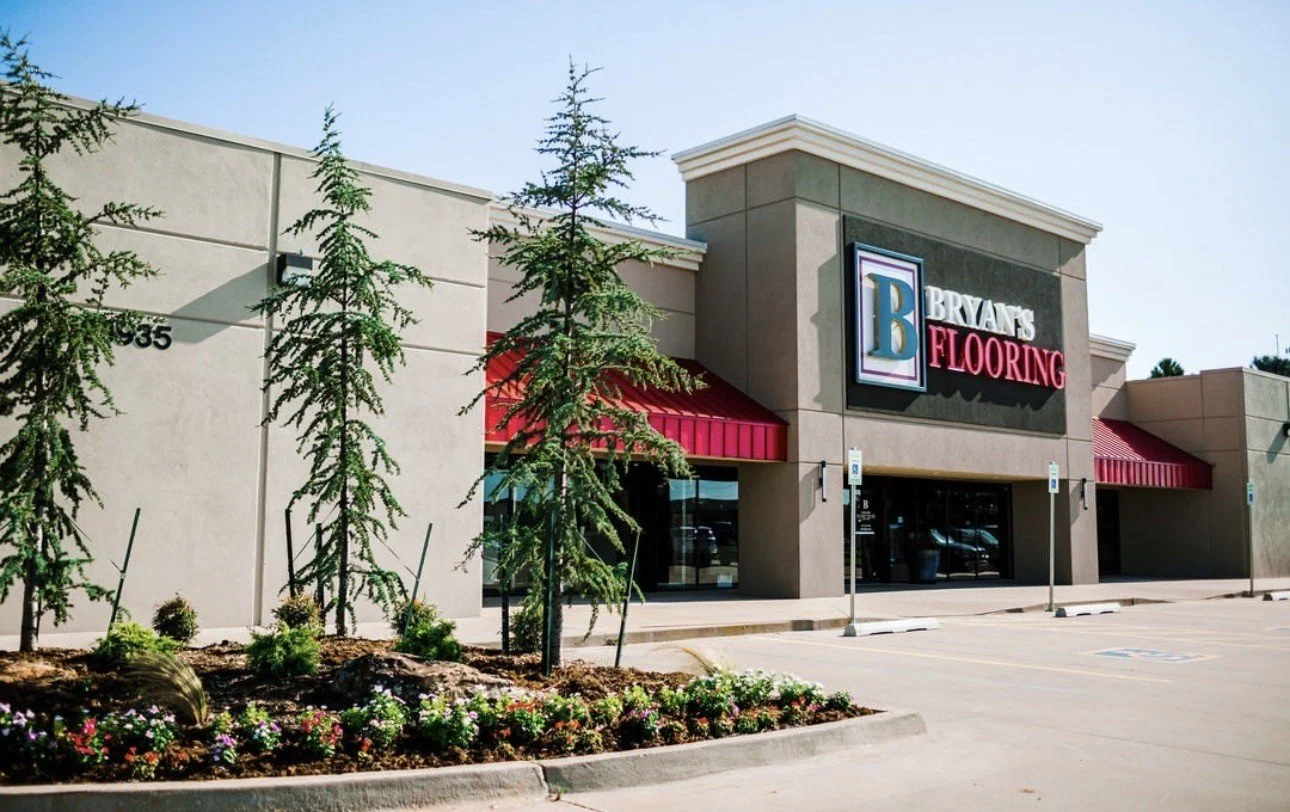 Bryan's Flooring store exterior with red awnings, landscaped flower bed, and parking lot