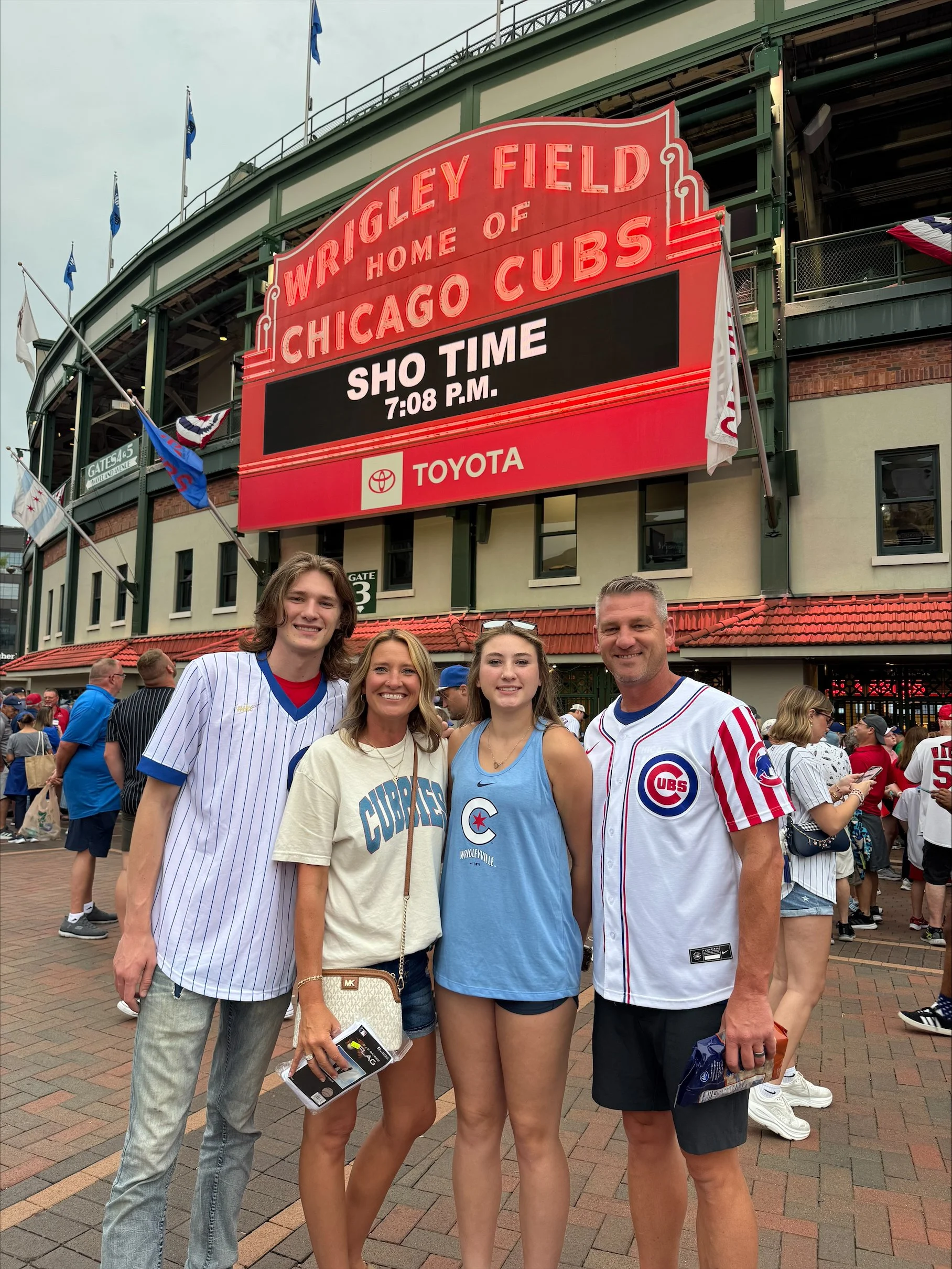Family posing outside Wrigley Field in Chicago beneath the marquee for a Chicago Cubs game.