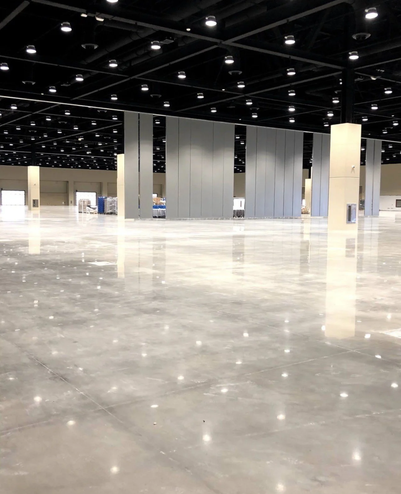 Empty convention center exhibition hall with polished concrete floors, partition walls, columns, and overhead lighting