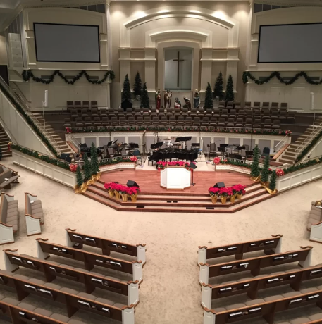 Decorated church sanctuary with a central pulpit, choir seating, grand cross, Christmas trees, poinsettias, and tiered pews.