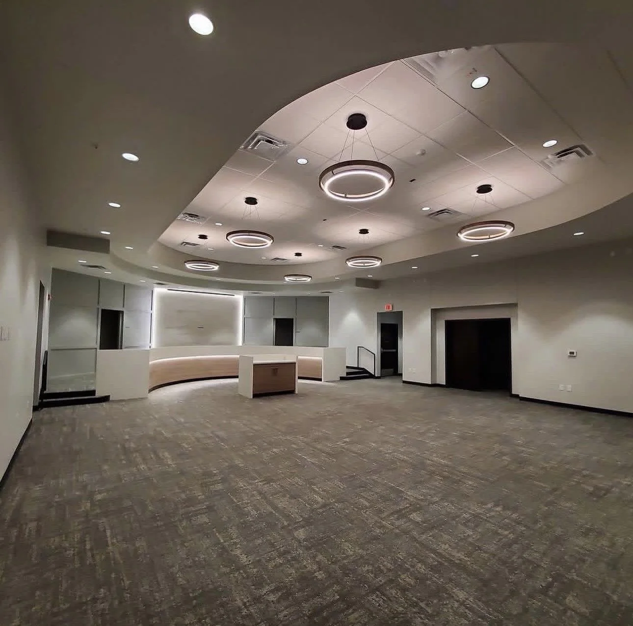 Modern commercial lobby with curved reception desk, gray carpet, circular pendant lights, and elevator doors