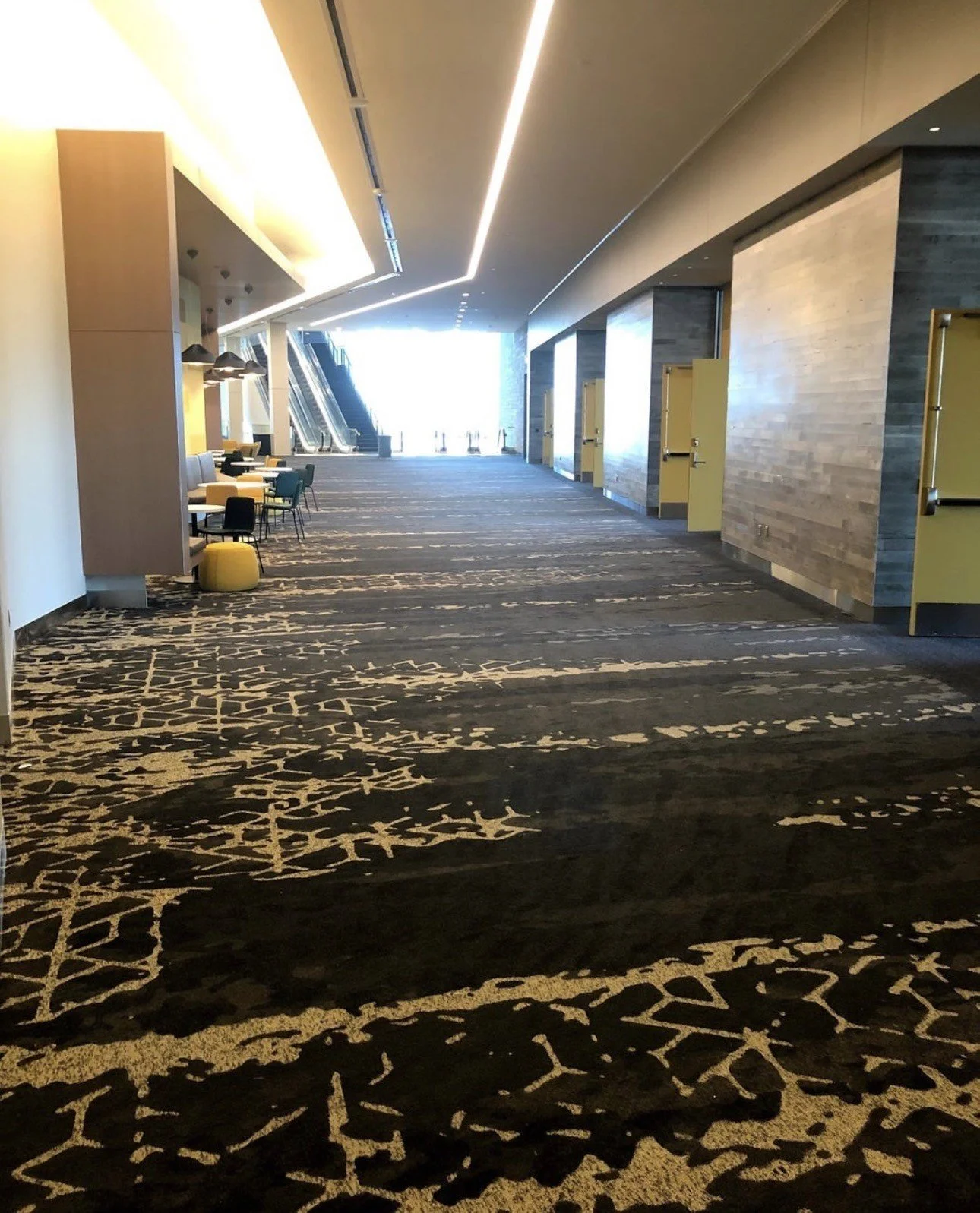Modern convention center hallway with patterned carpet, lounge seating, escalators, and restroom doors