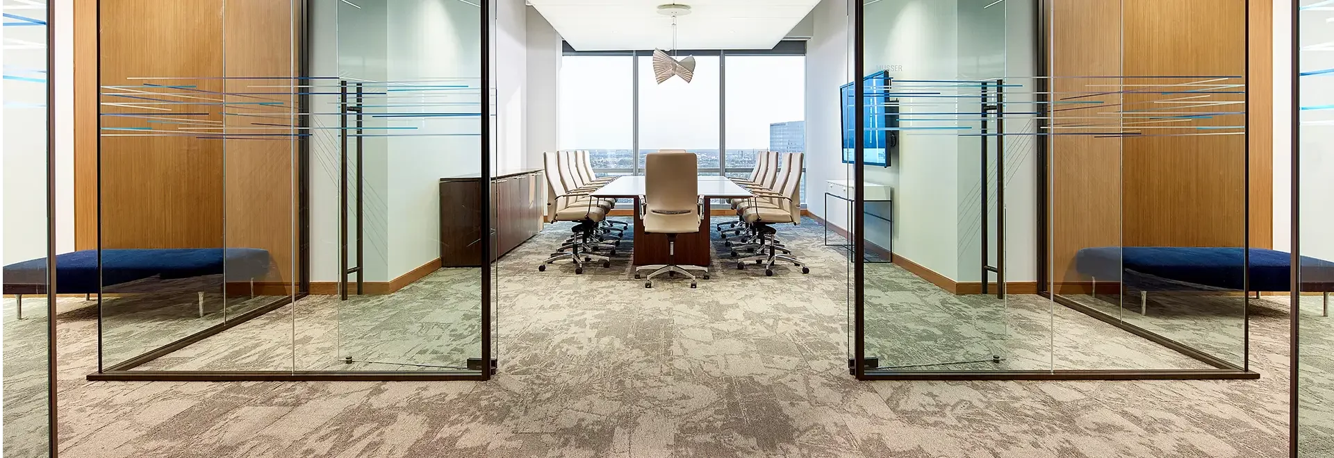 Modern glass-walled executive conference room with a long table, leather chairs, city views, and mirrored lounge areas