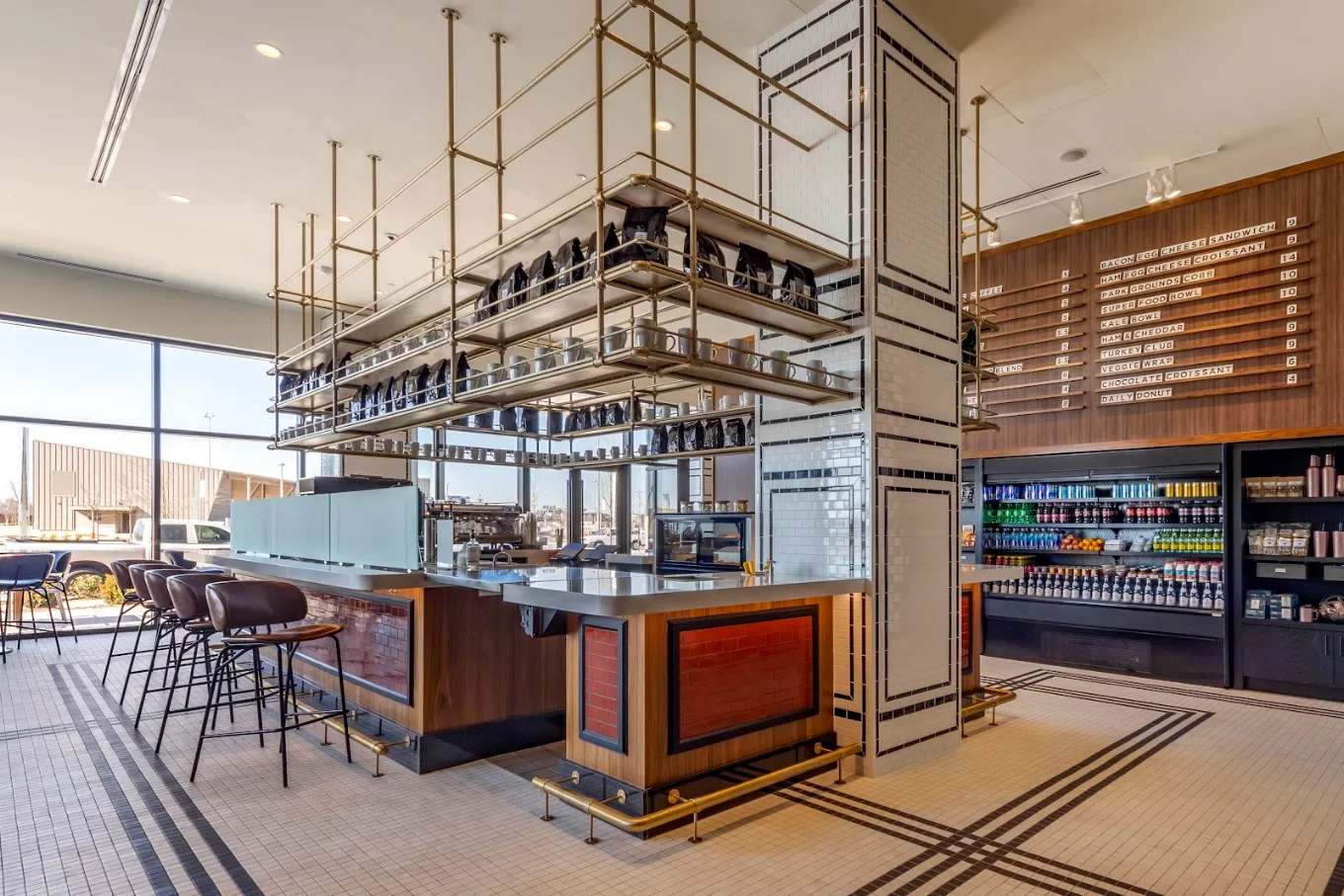 Modern cafe interior with brass shelving, tiled column, counter seating, beverage refrigerator, and menu board