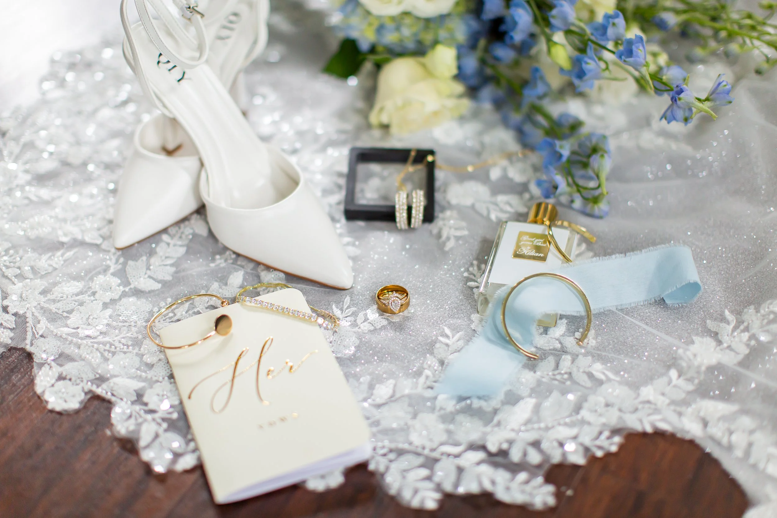White wedding shoes, jewelry, and flowers arranged on a lace-covered table at a wedding celebration.