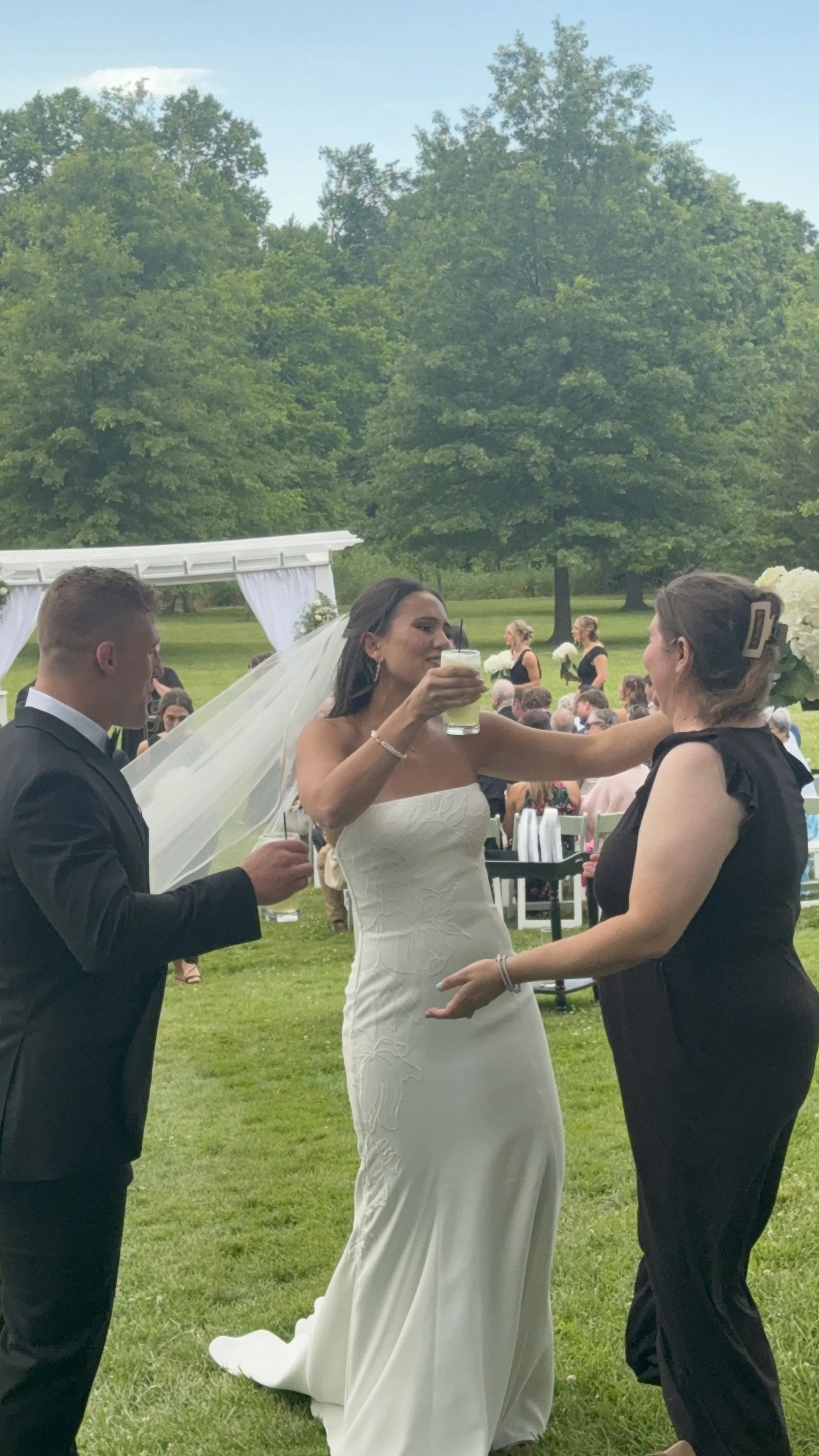 Bride and groom talking with a woman at an outdoor wedding reception.