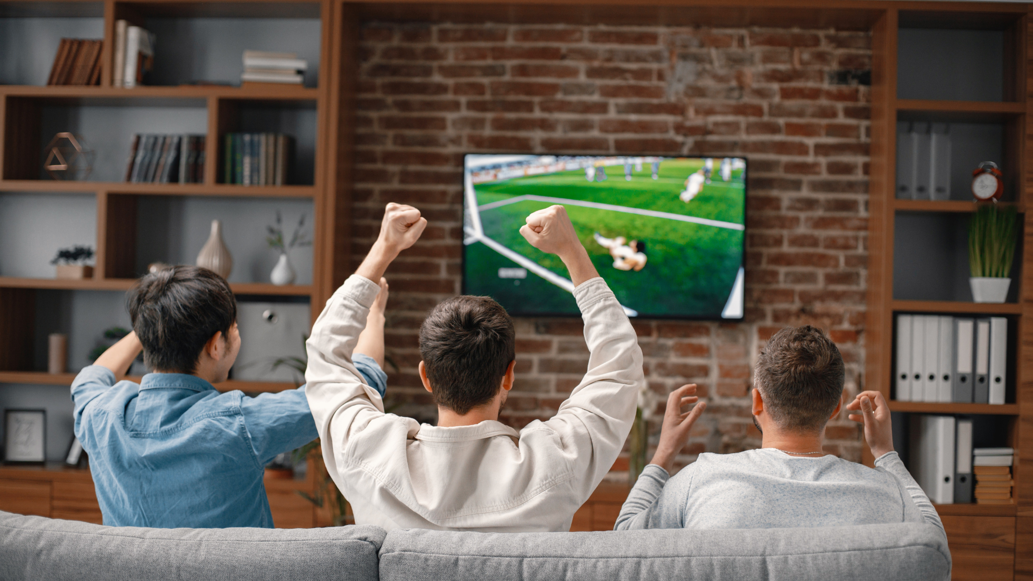 Group of young men watching and celebrating a soccer game on a TV in a modern living room.