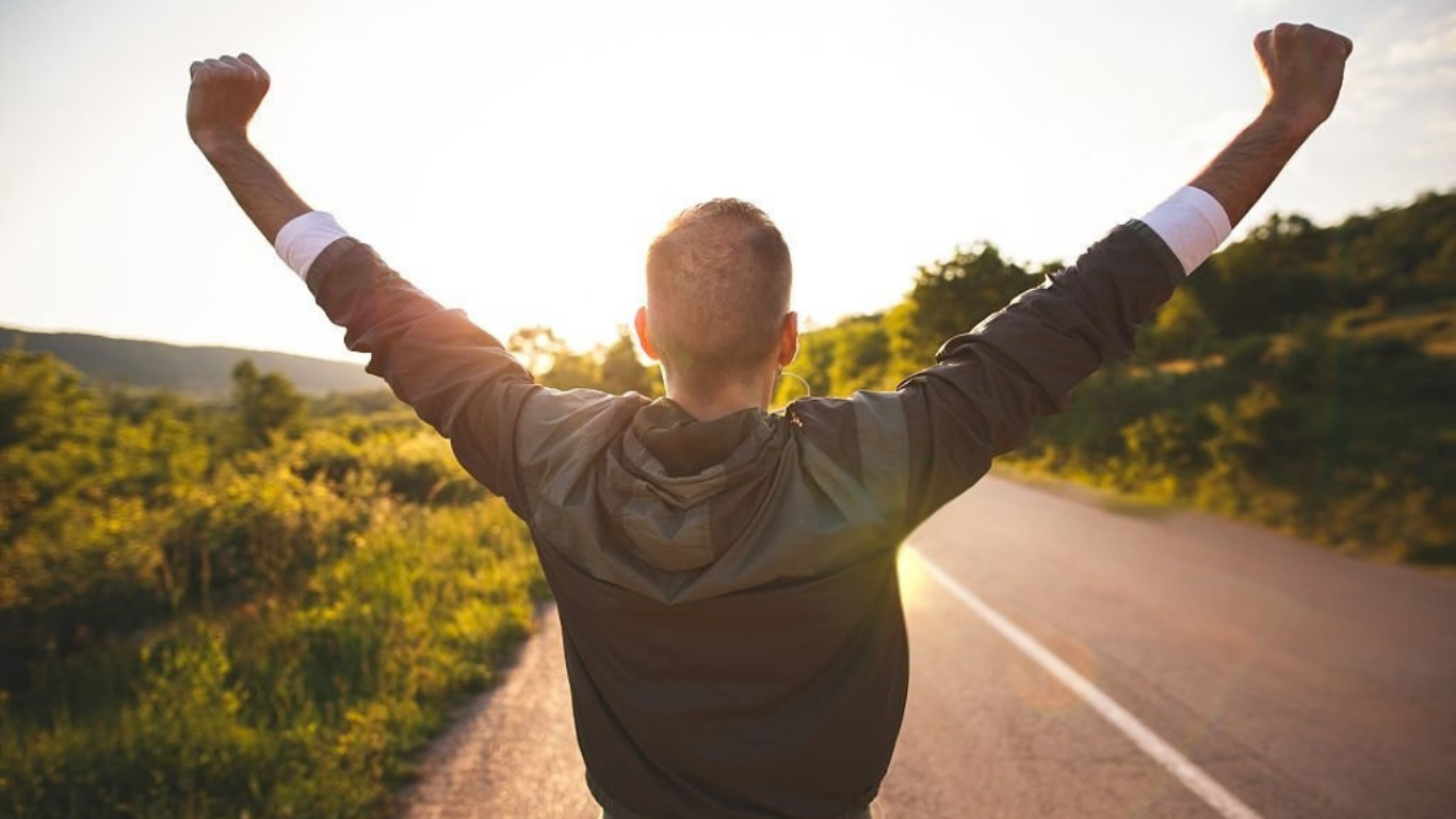 Person with arms raised celebrating on an open road during sunset.