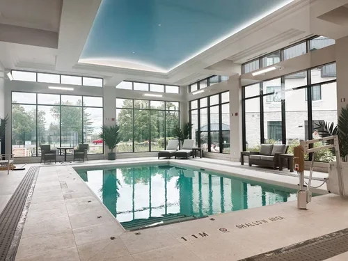Indoor swimming pool area with lounge chairs and large windows showing outdoor greenery.