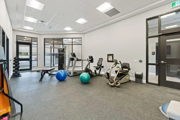 Empty fitness room with exercise equipment including a treadmill, stationary bikes, stability balls, and a weight bench.