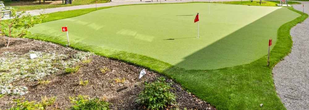 Miniature golf course green with flags and surrounding garden beds.