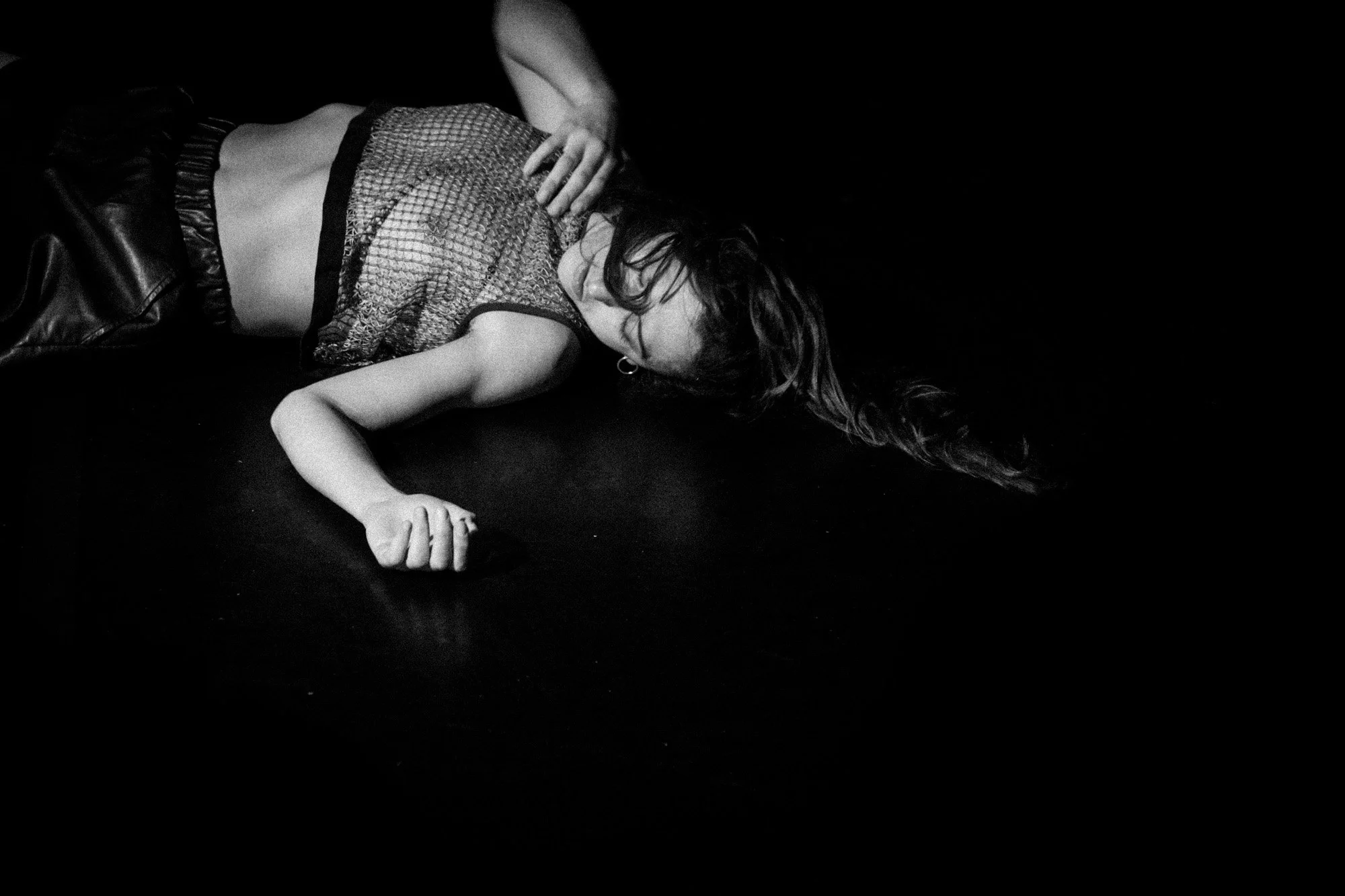 Black-and-white photograph of a performer lying on their side on a dark stage.