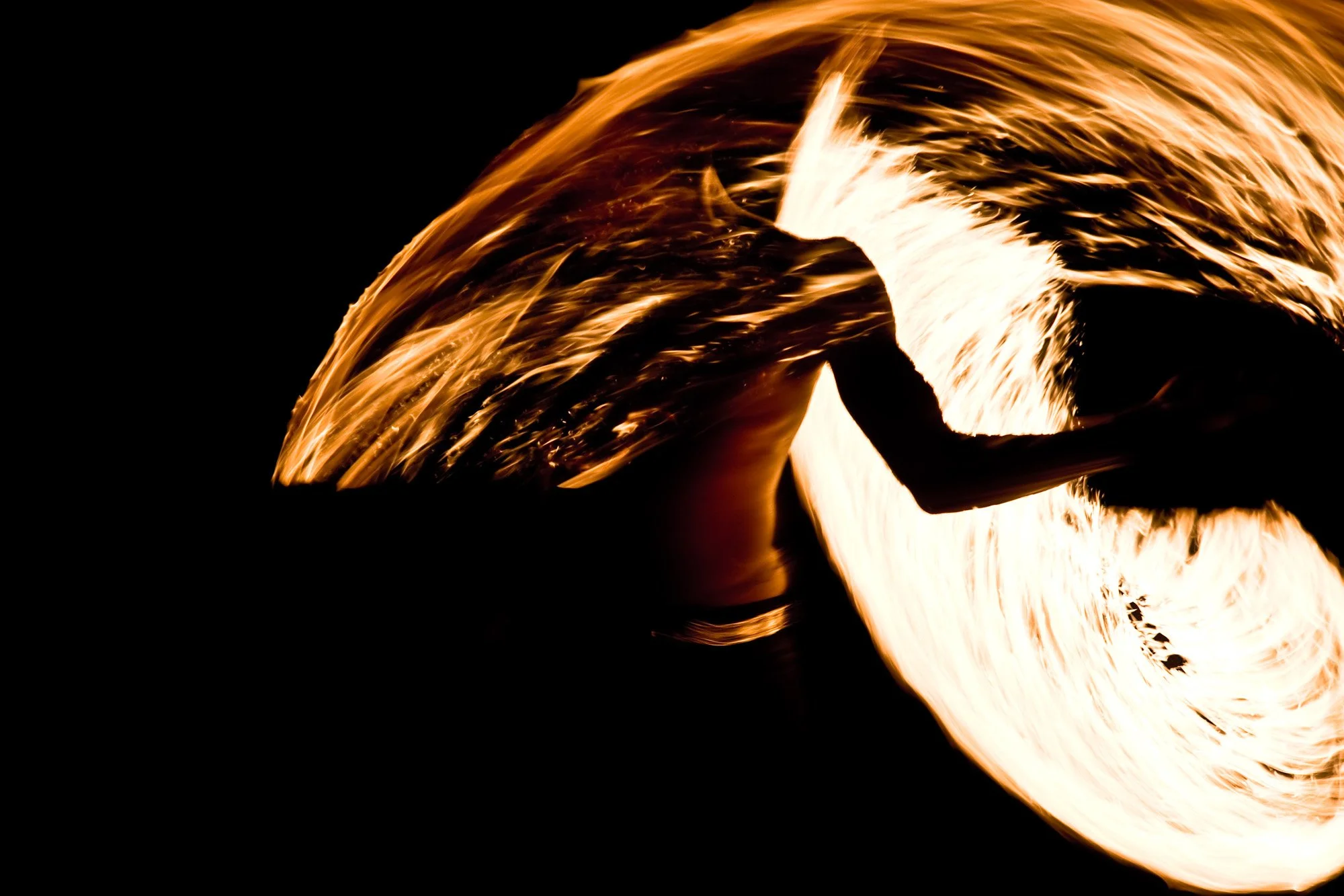 A fire performer surrounded by bright arcs of flame against the darkness.