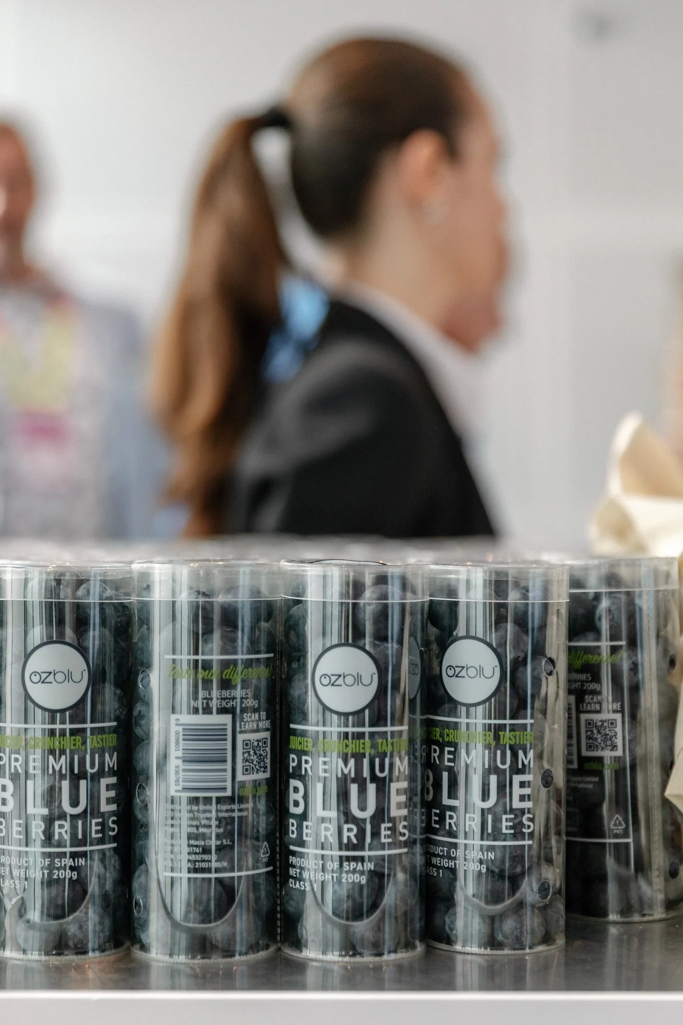 Clear packs of OZblu blueberries displayed at Berry Congress, with visitors in the background.