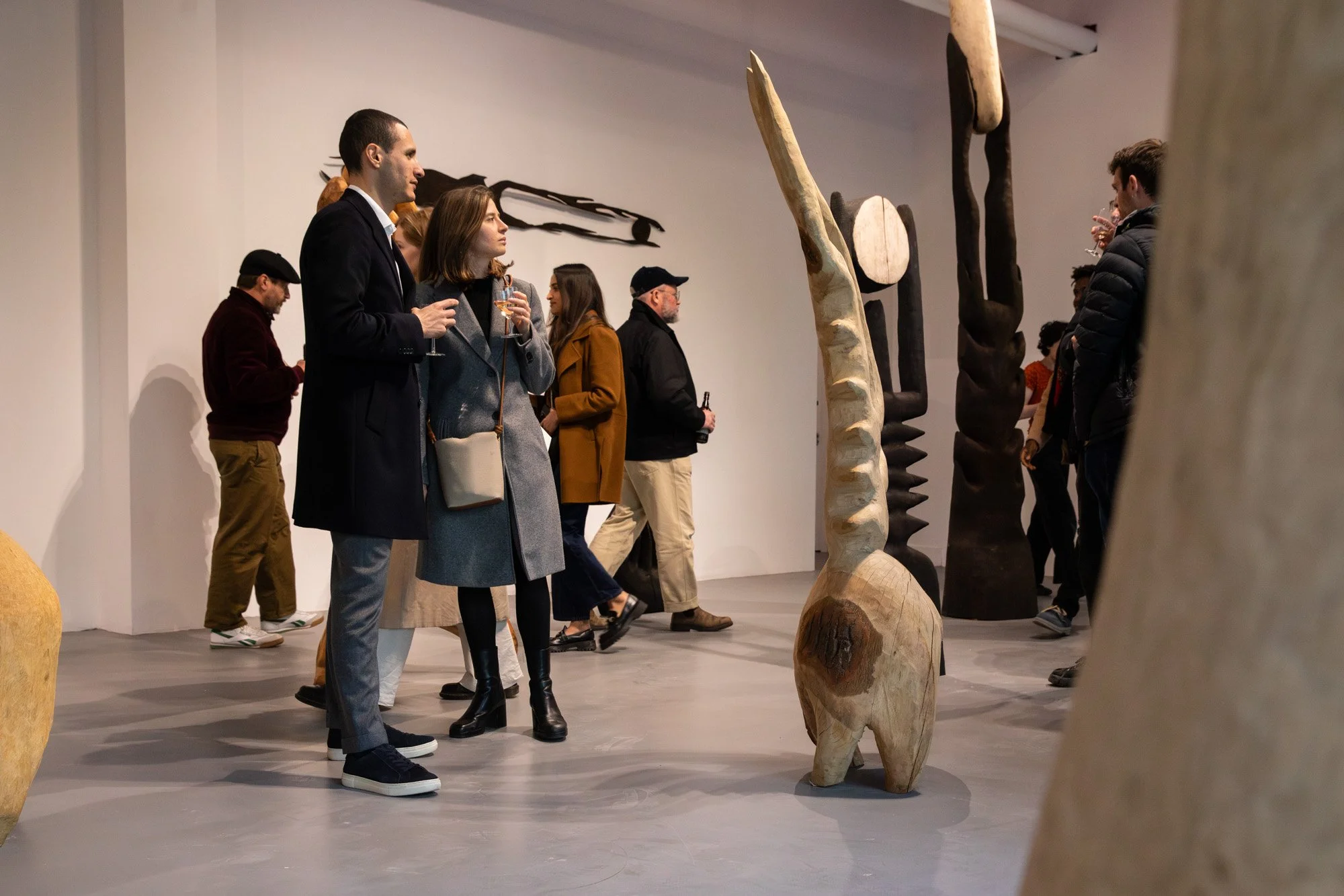 Two visitors looking at an artwork while holding drinks at a Sol Bailey Barker exhibition.