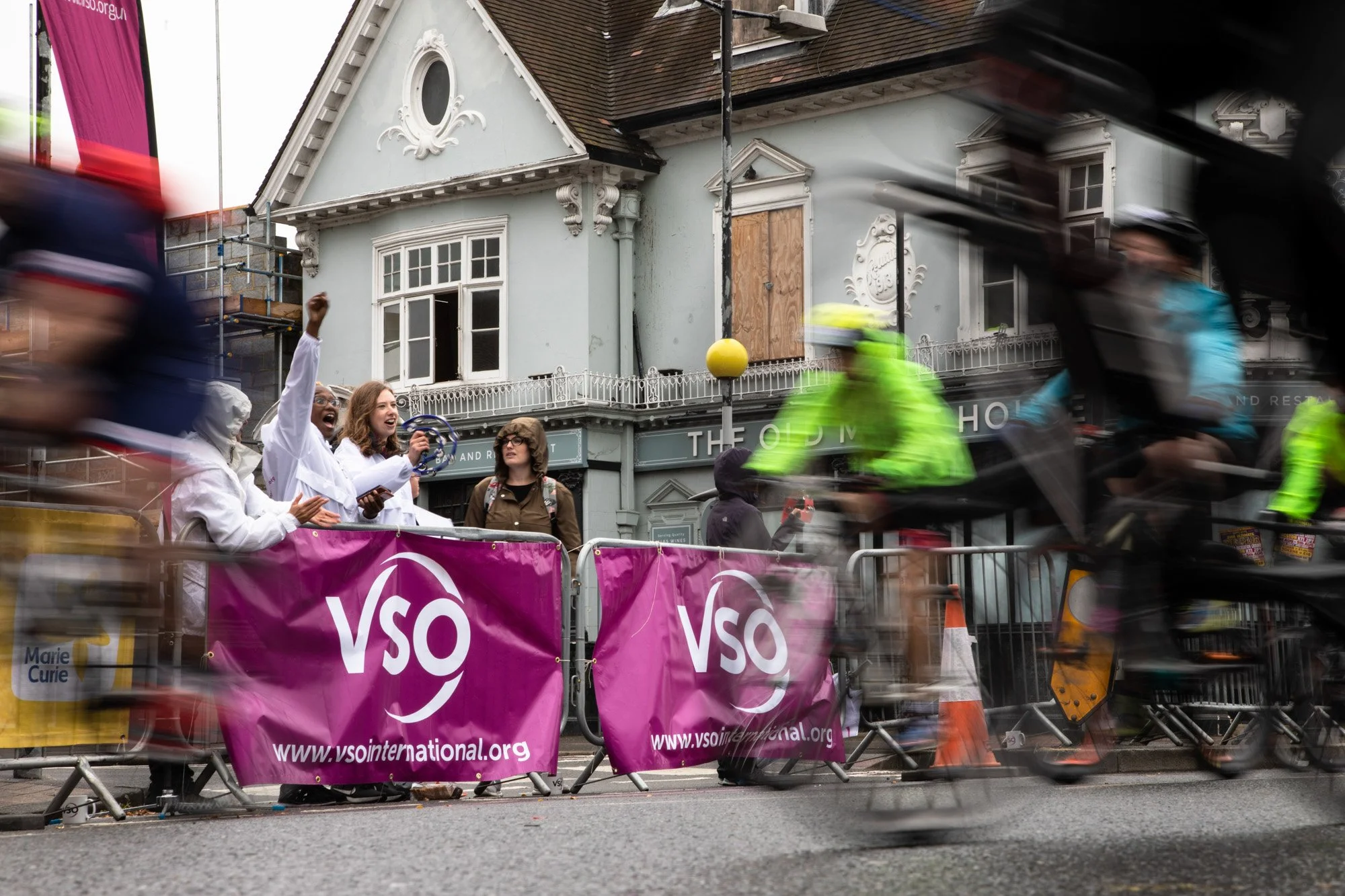Cyclists speeding past VSO supporters behind purple roadside banners at RideLondon.