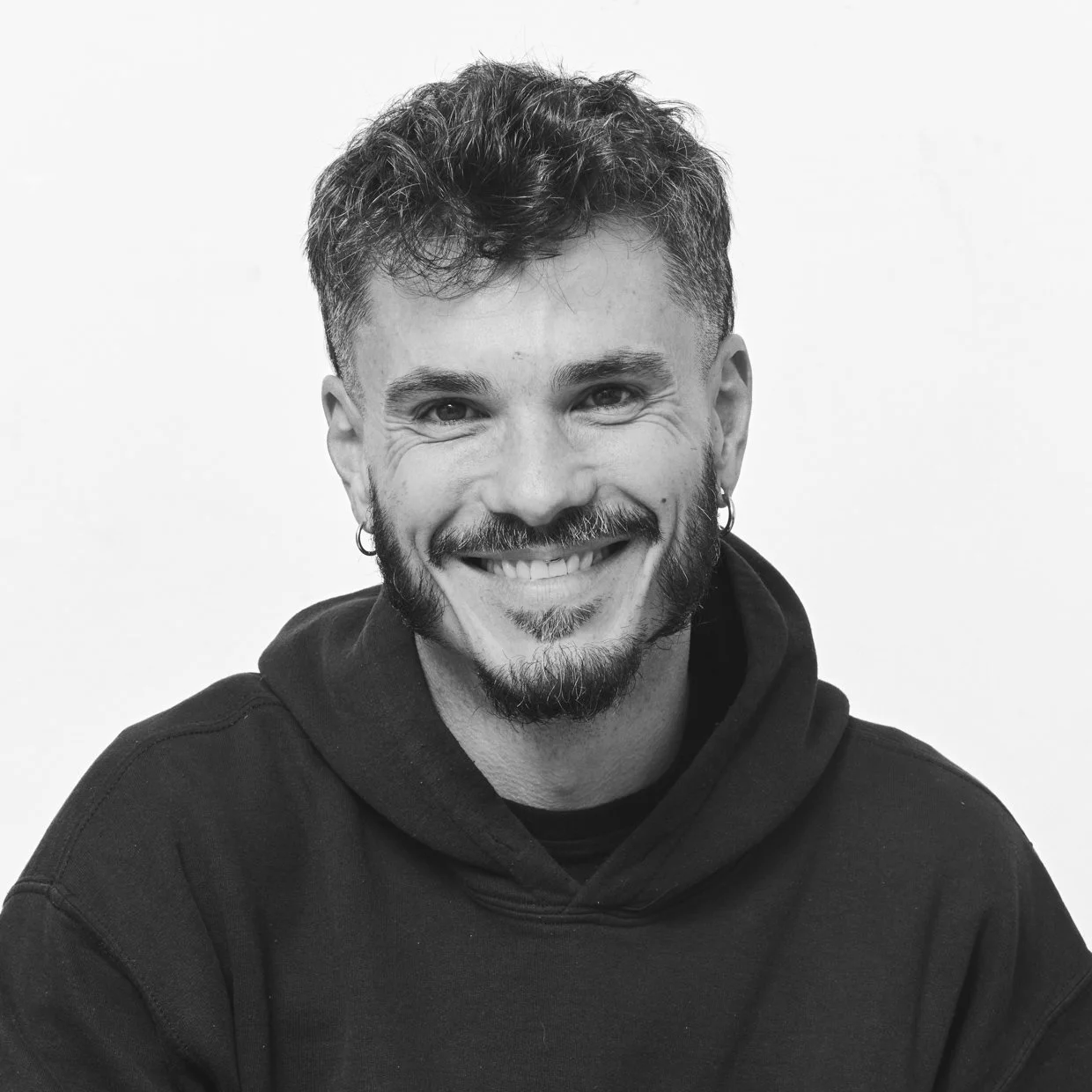 Black-and-white portrait of Manu Valcarce, founder of MVV Media, smiling in a dark hoodie.