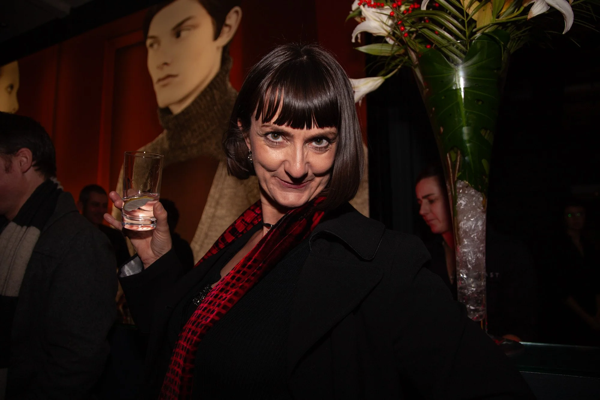 A guest holding a drink beside floral decorations at an awards reception.