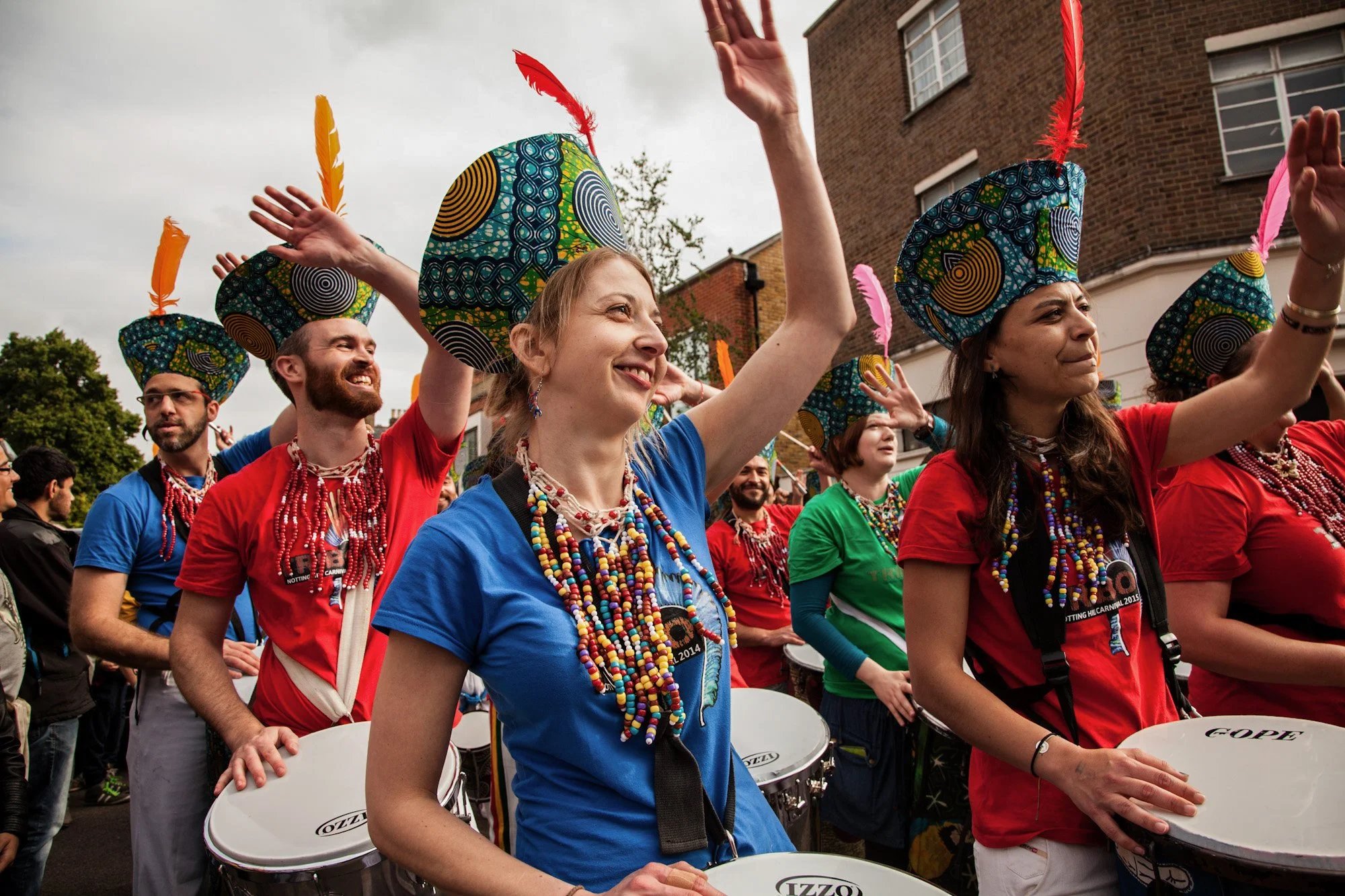 Drummers in bright costumes raising their hands during a street performance at La Clave festival.