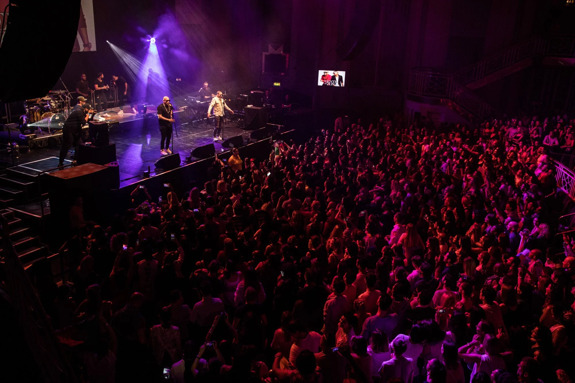A large concert audience watching performers on a stage lit in purple.